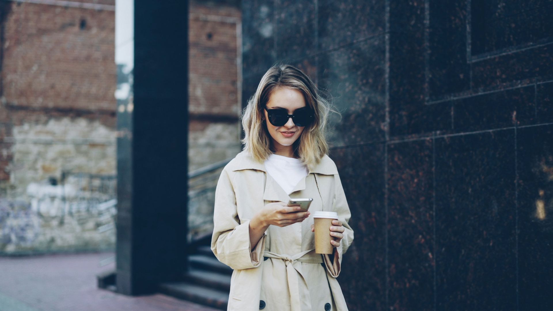 Woman with coffee and phone on city street
