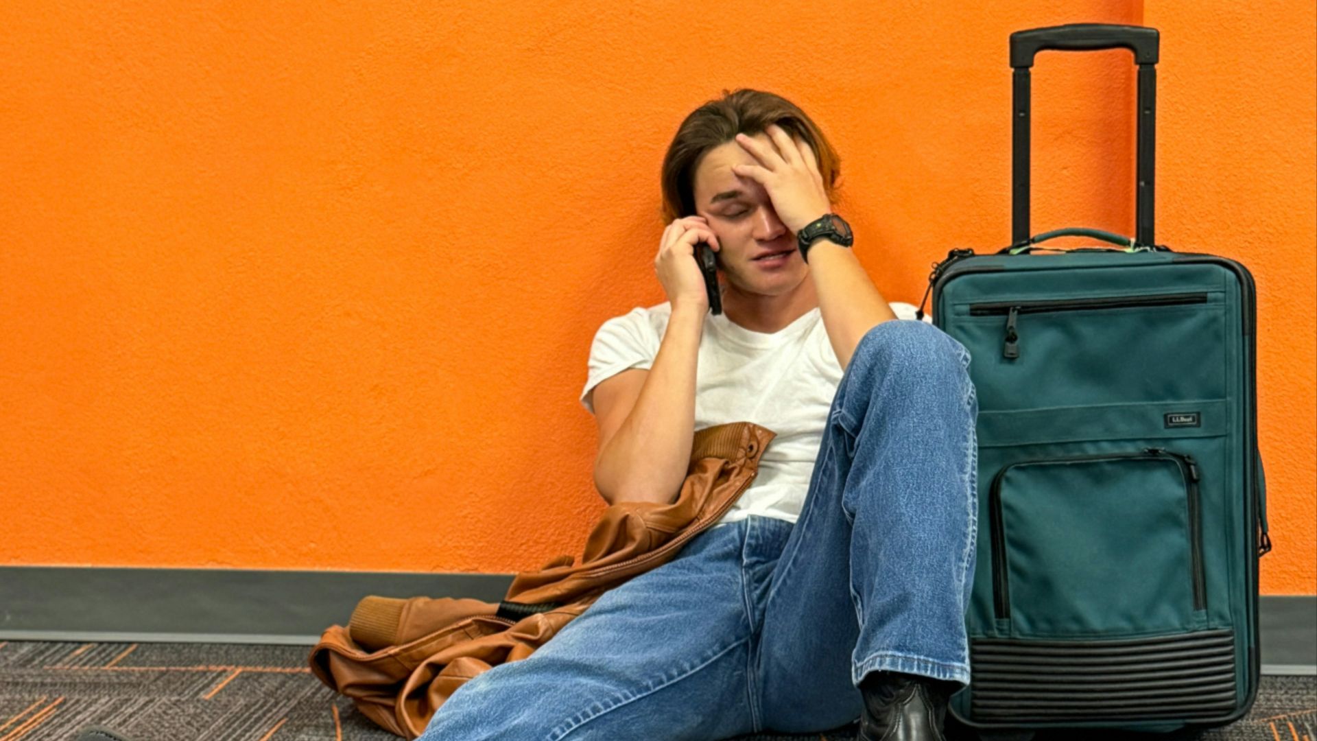 Man sitting on floor with suitcase, looking distressed.