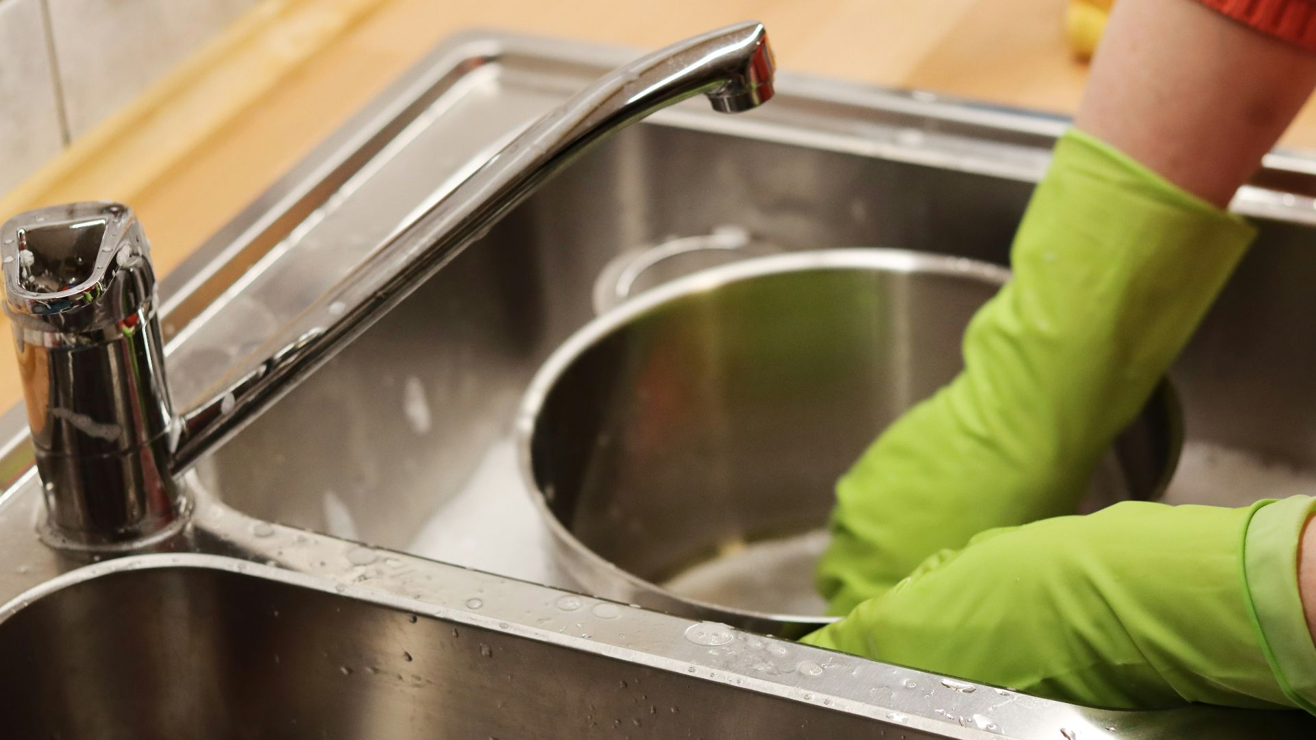 person in green long sleeve shirt washing stainless steel sink
