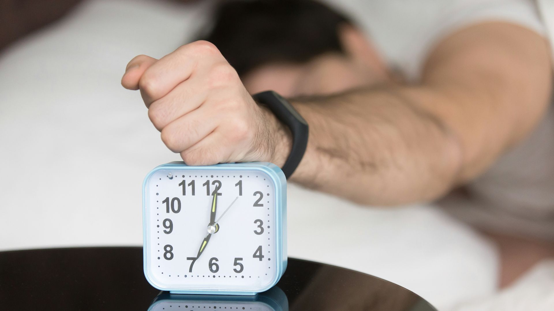 A man laying in bed with a clock on top of him