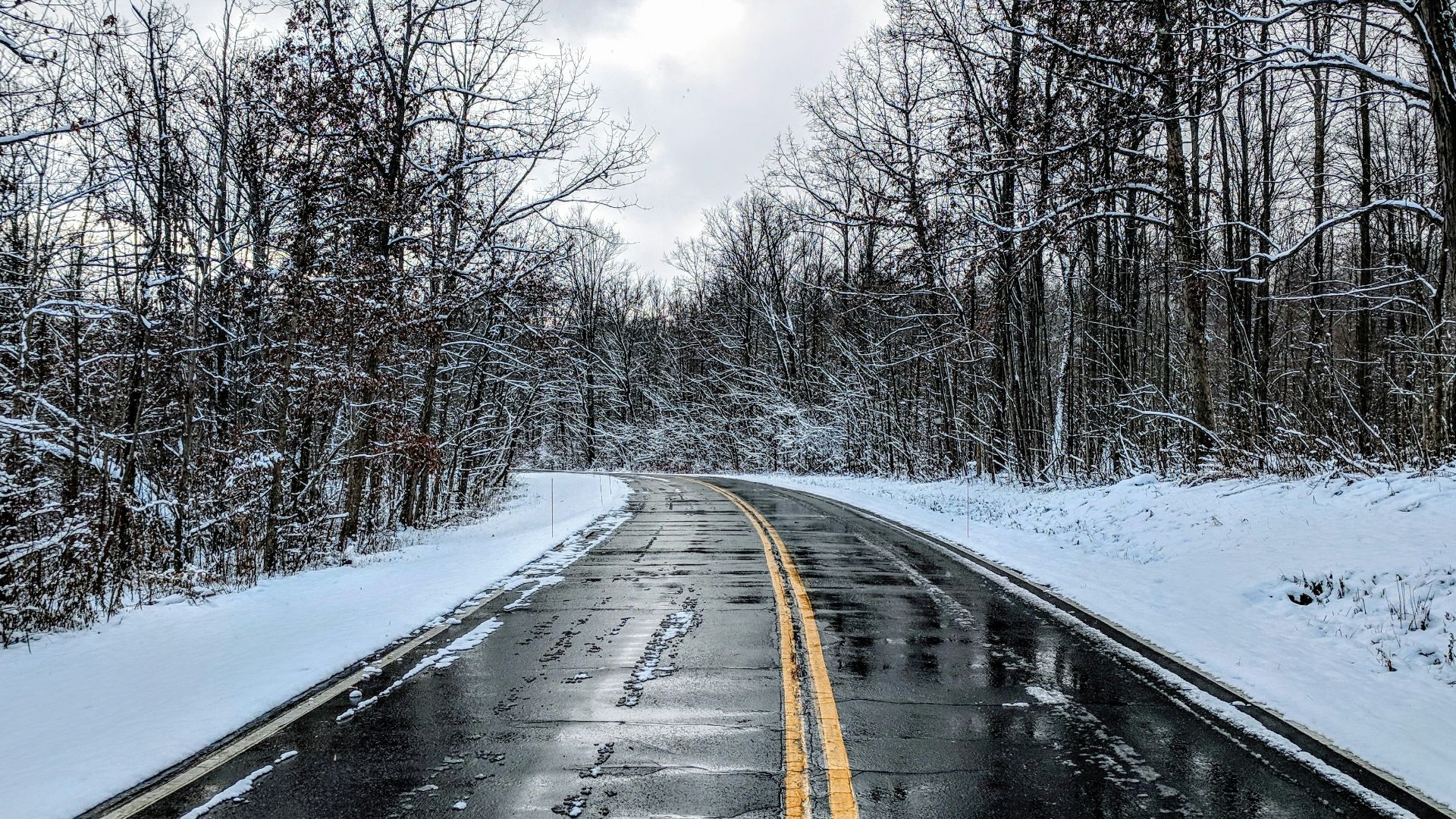 empty highway with solid double yellow line in between snow covered ground at daytime