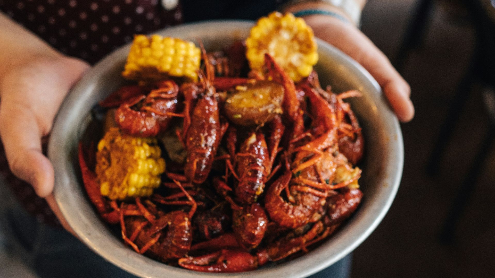 person holding bowl of shrimp with slice of corn dish