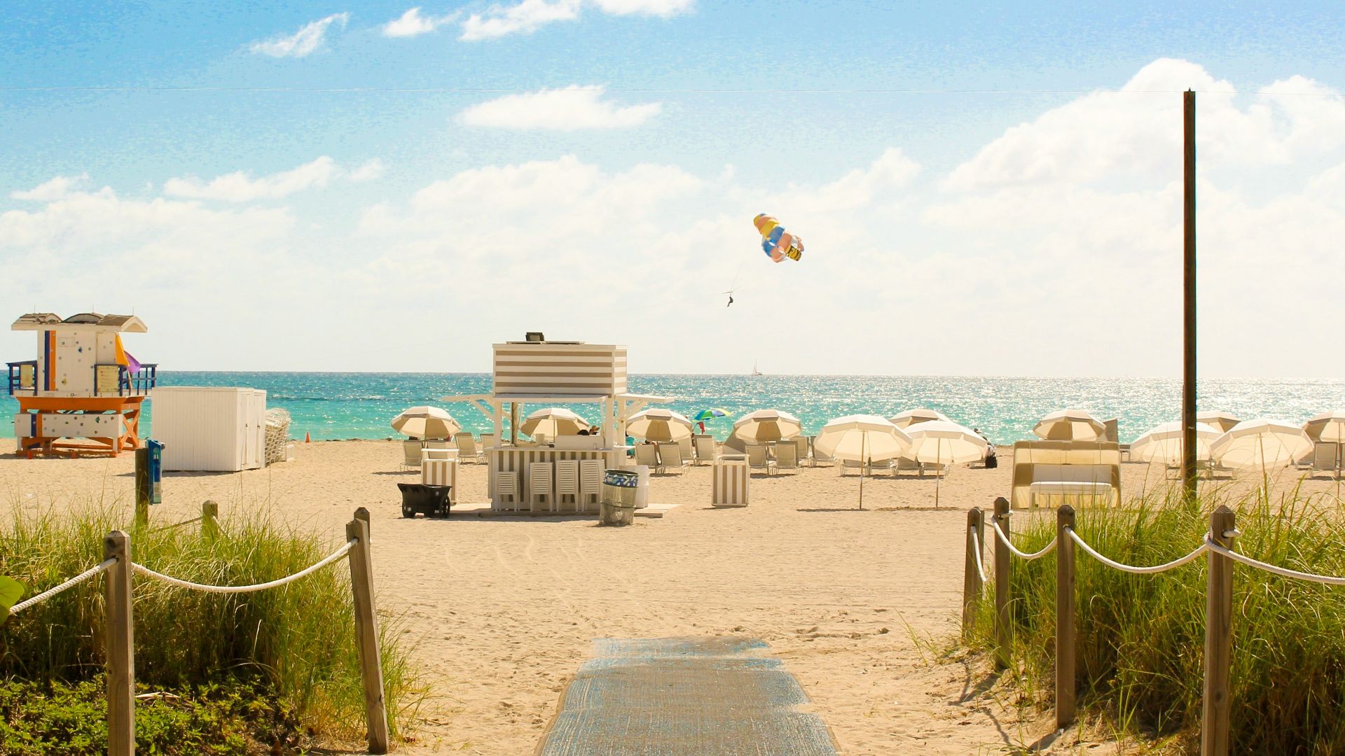 gray pathway leading to parasol, lifeguard house, and sea a daytime