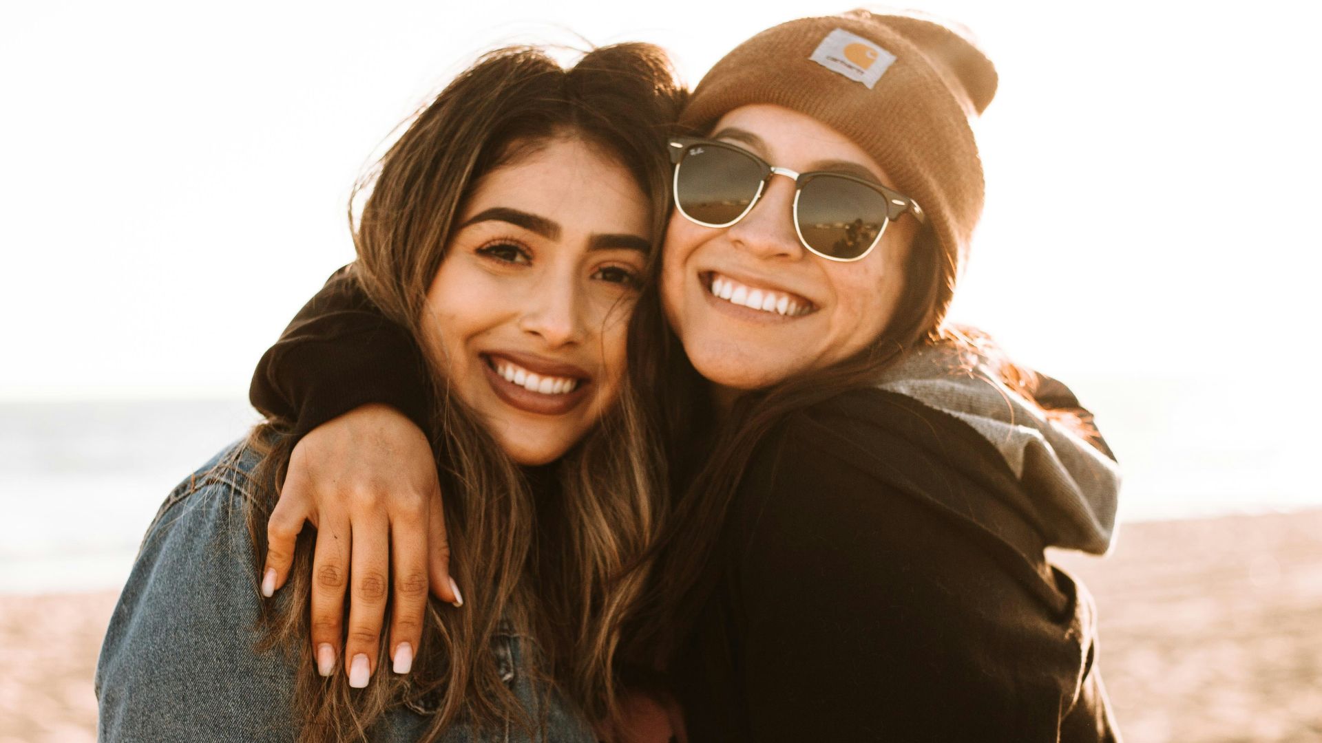 woman hugging other woman while smiling at beach