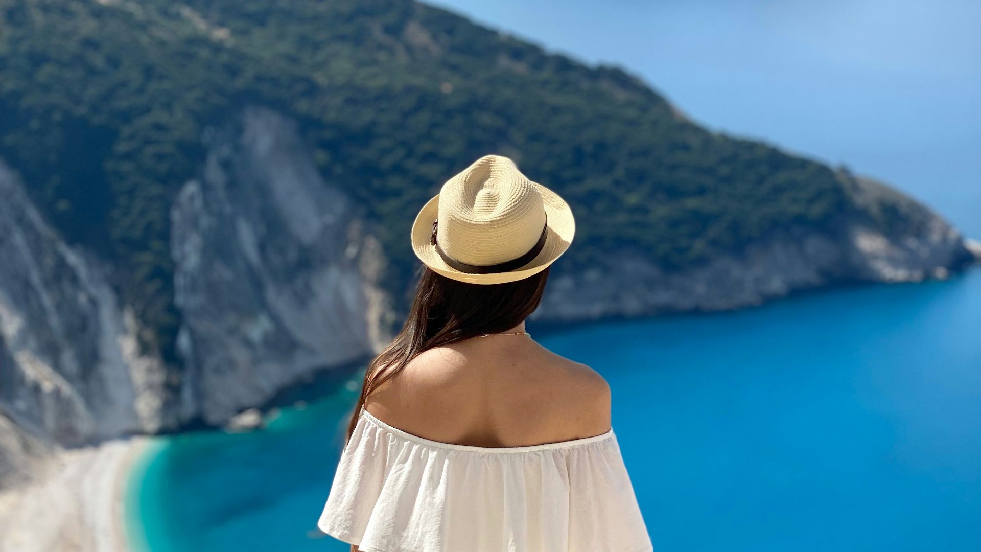 a woman in a white dress and hat looking at the ocean