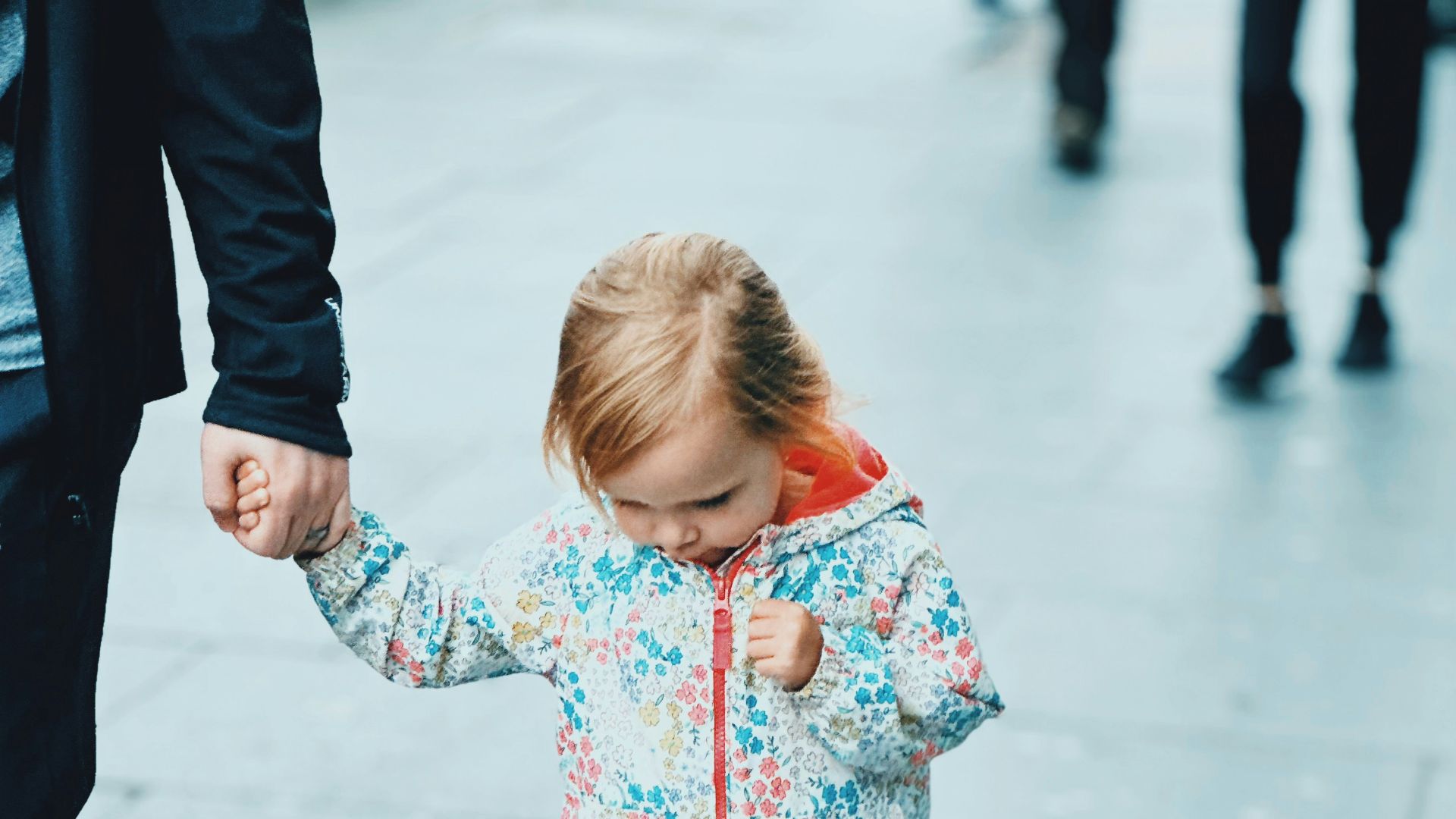 A young girl holds a hand while walking on pavement.