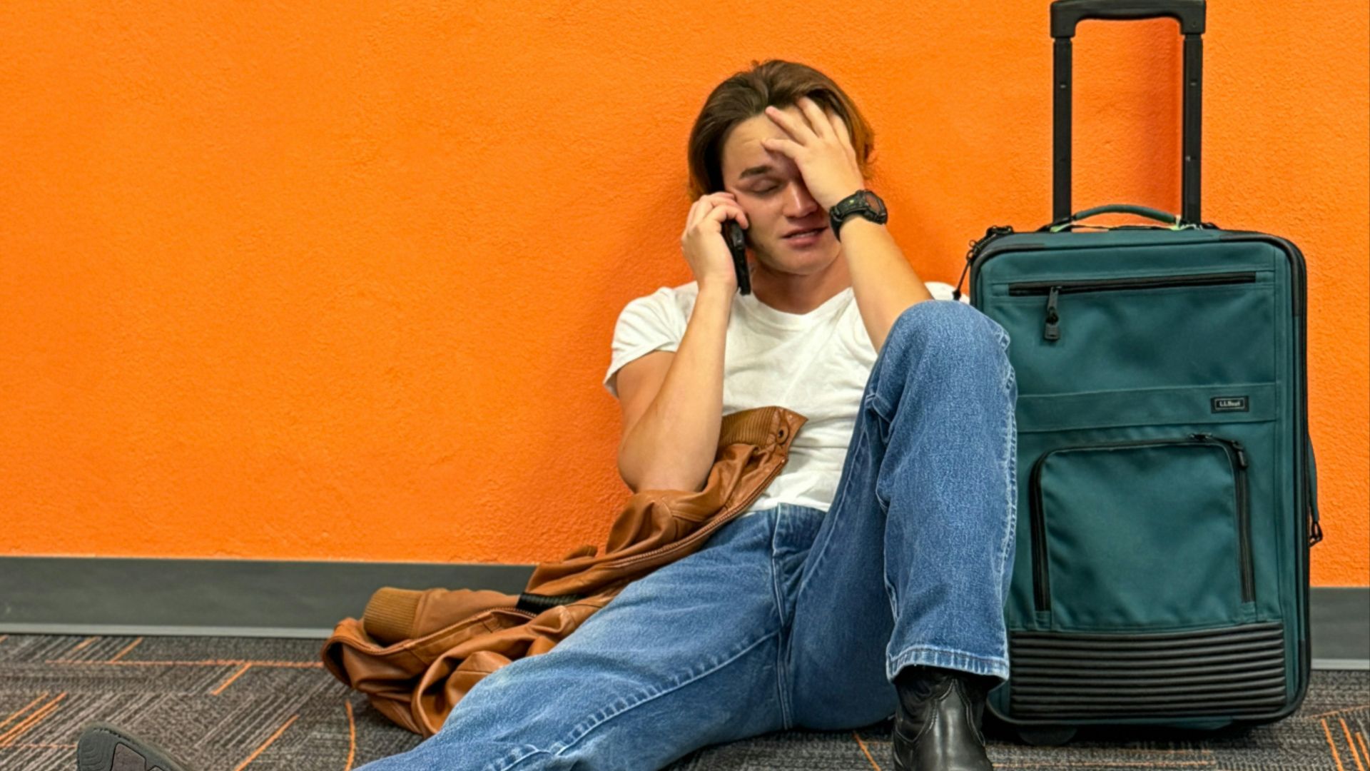Man sitting on floor with suitcase, looking distressed.