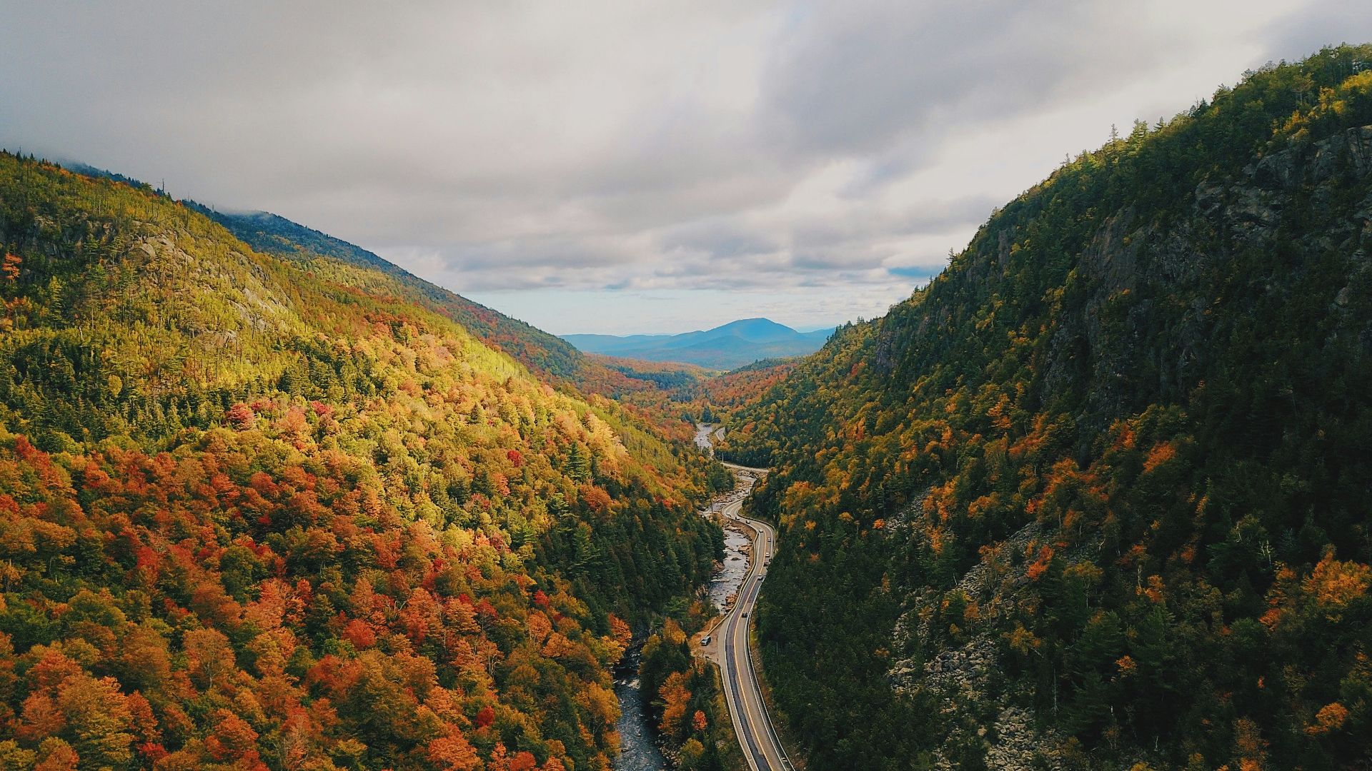 gray concrete road between green and brown mountains under white cloudy sky during daytime