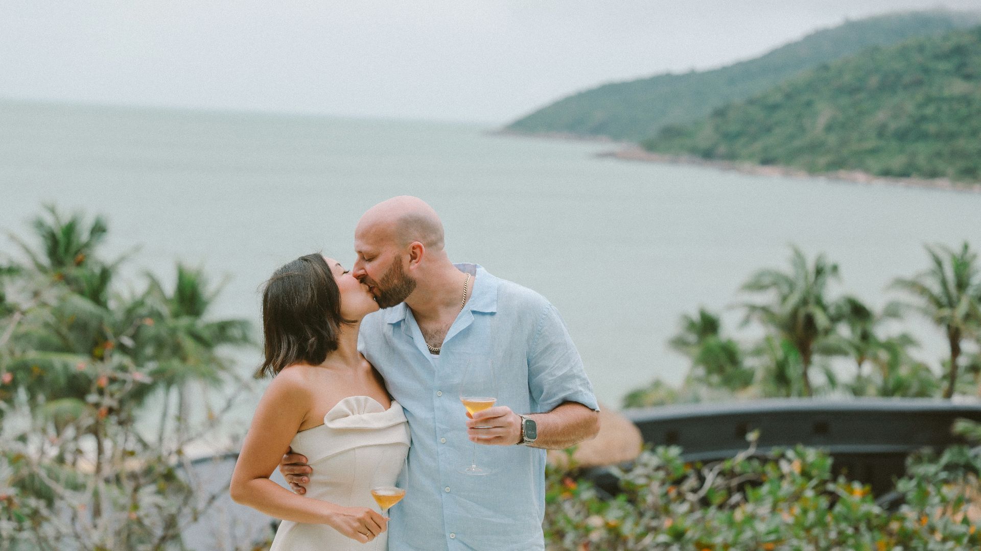Couple kissing with drinks by the ocean.