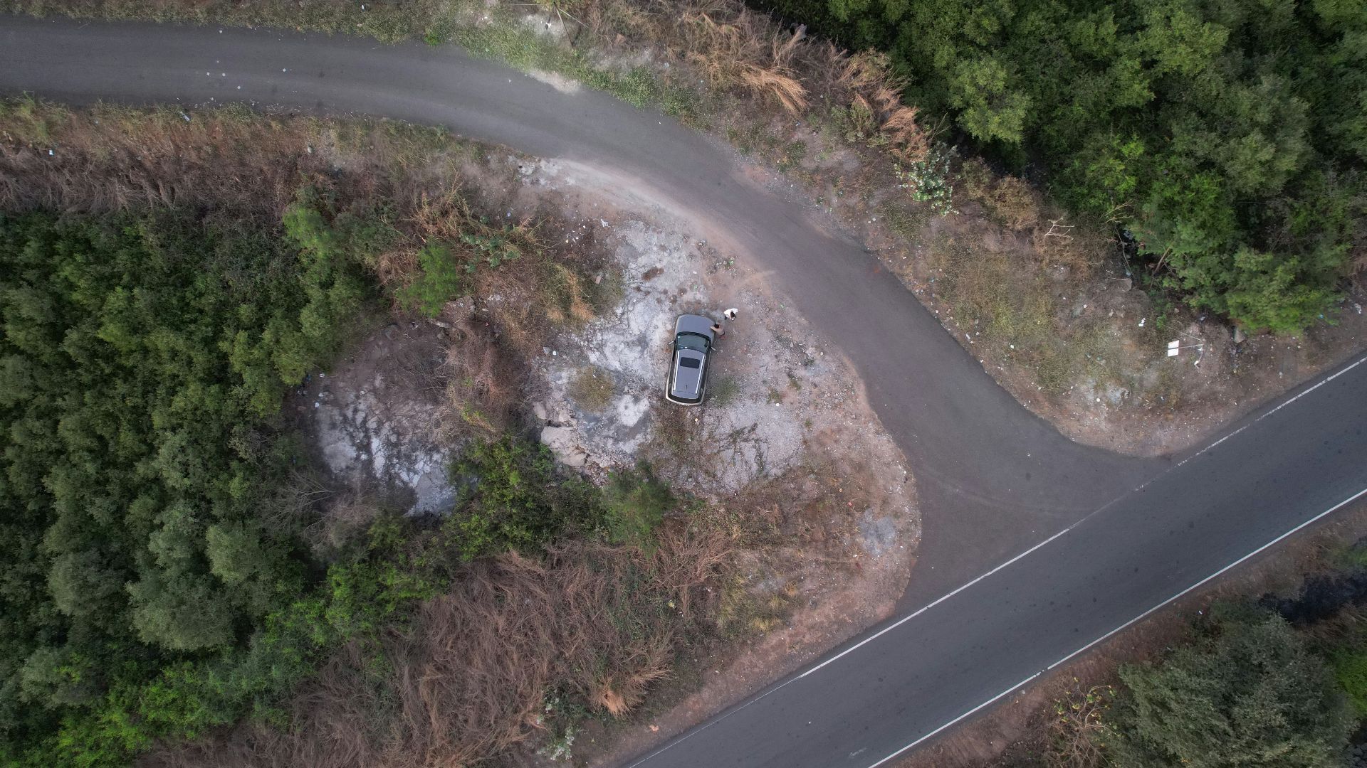 an aerial view of a car parked on a road in the middle of a forest