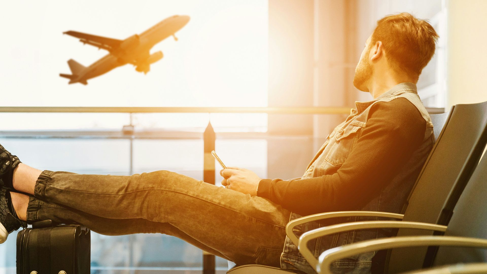 man sitting on gang chair with feet on luggage looking at airplane