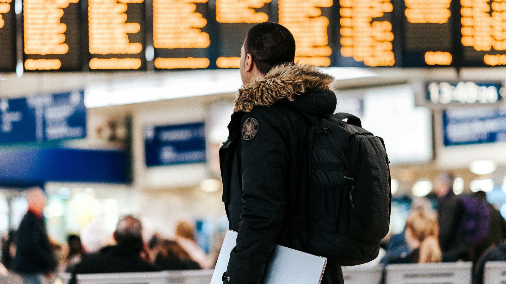 man standing inside airport looking at LED flight schedule bulletin board