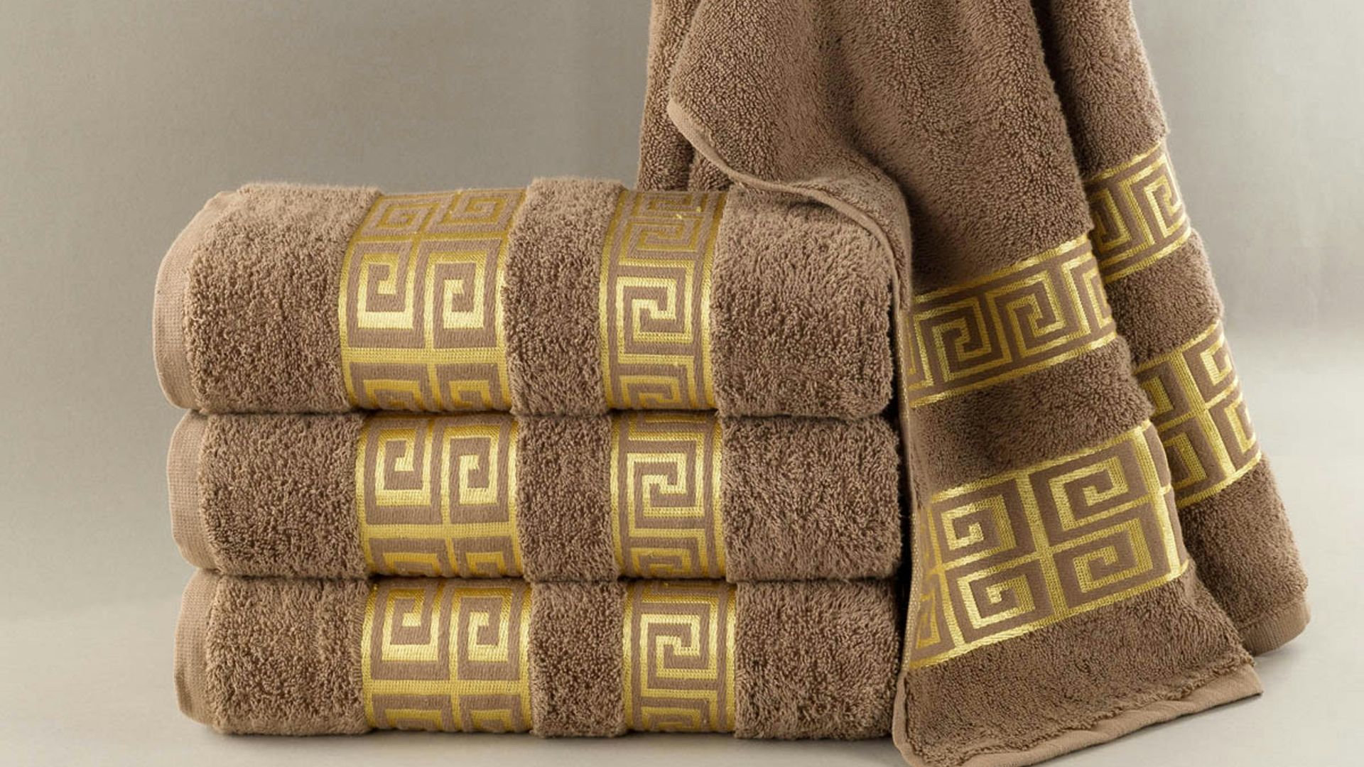 Stack of brown towels with gold greek key pattern.