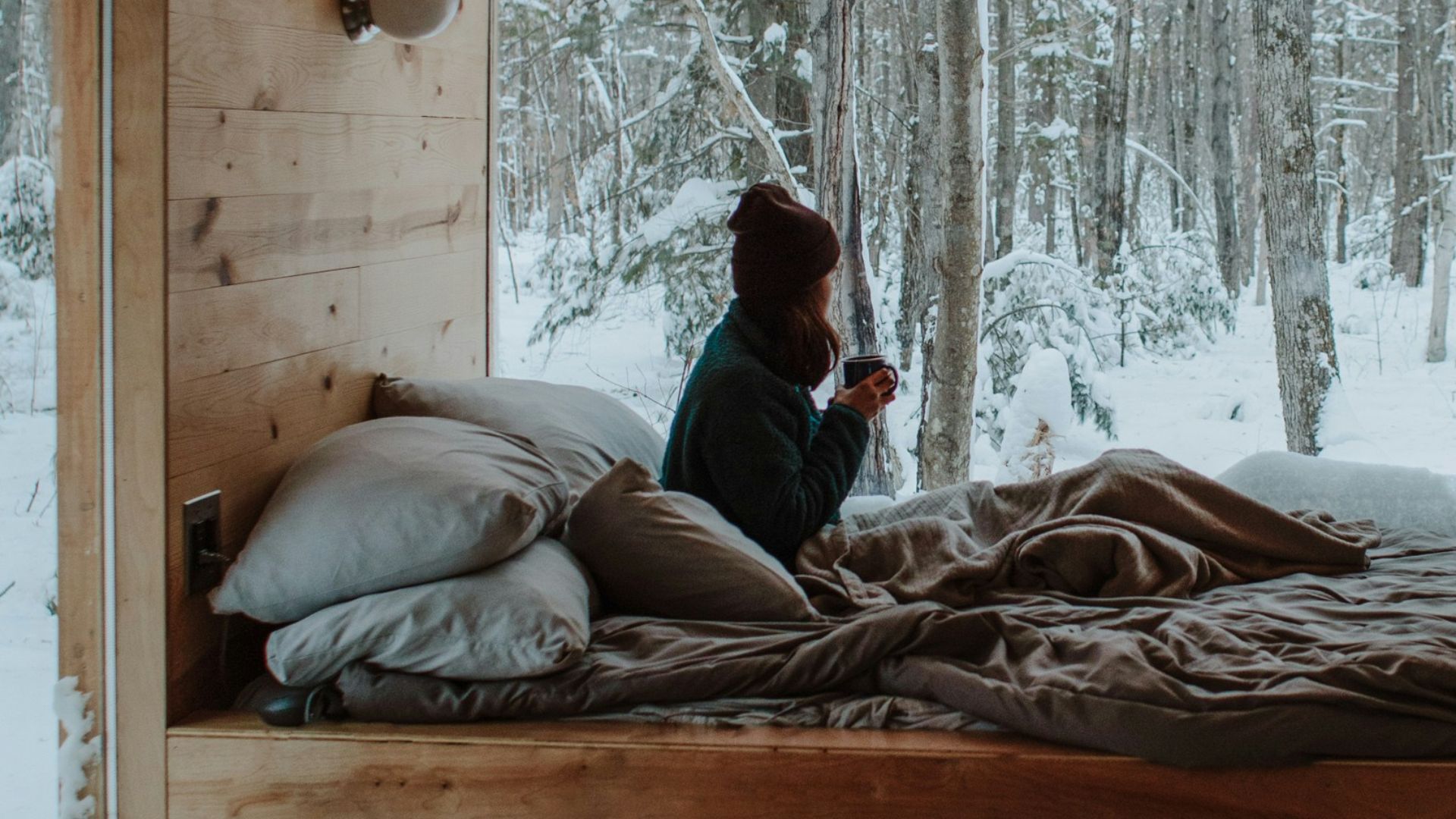 woman sitting on bed watching by the window during winter