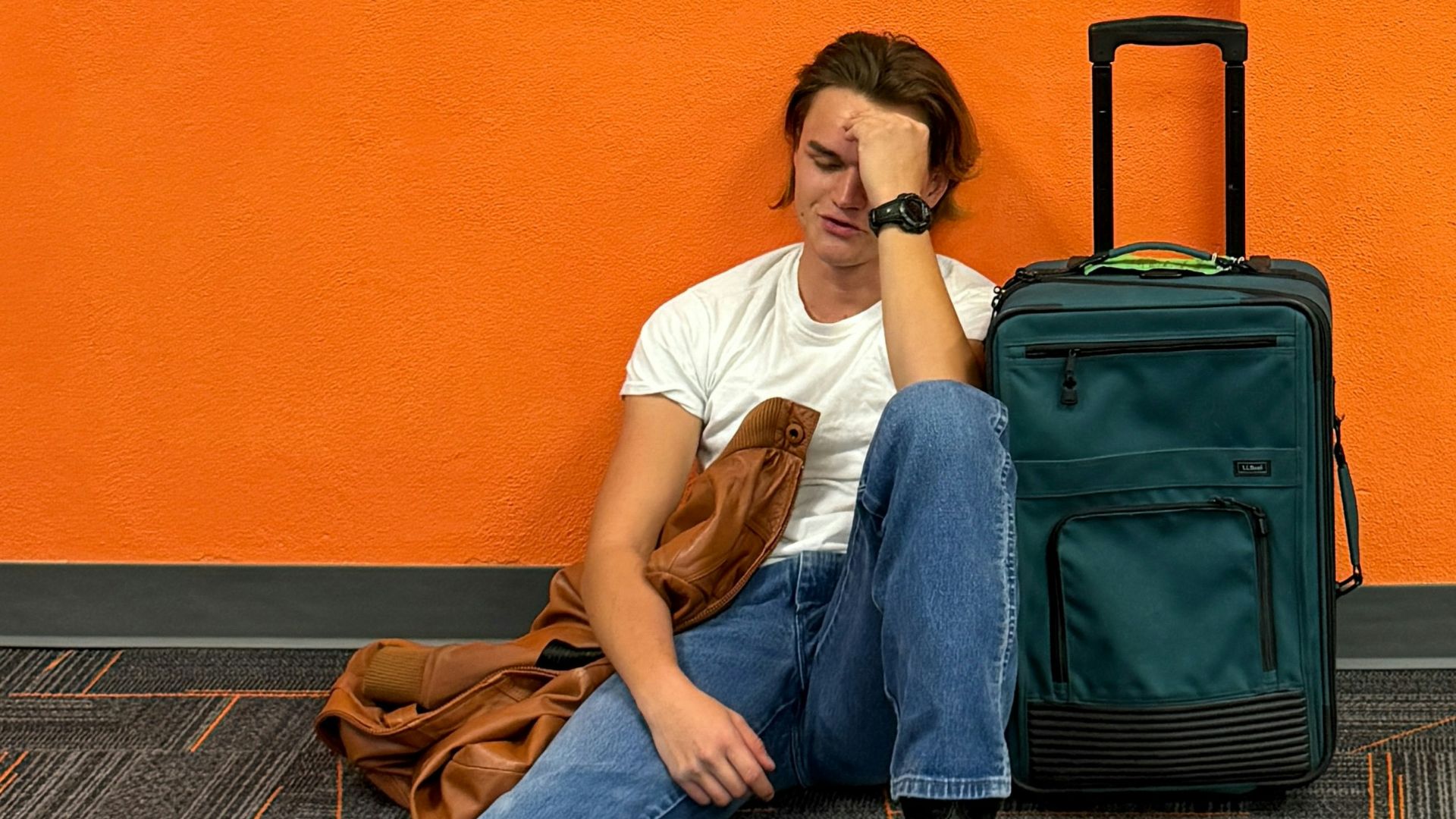 Man sitting on floor with luggage, looking tired.