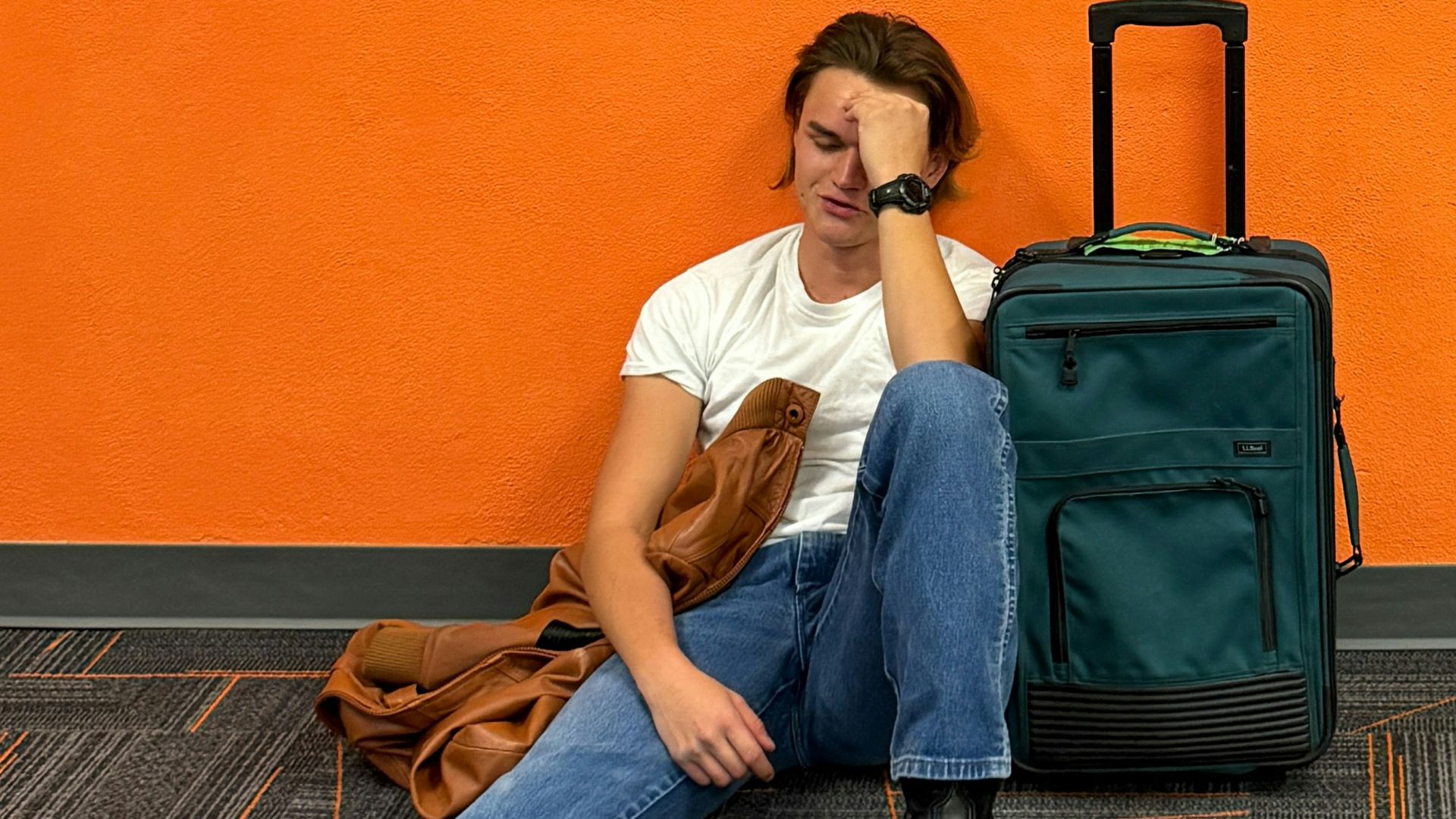 Man sitting on floor with luggage, looking tired.