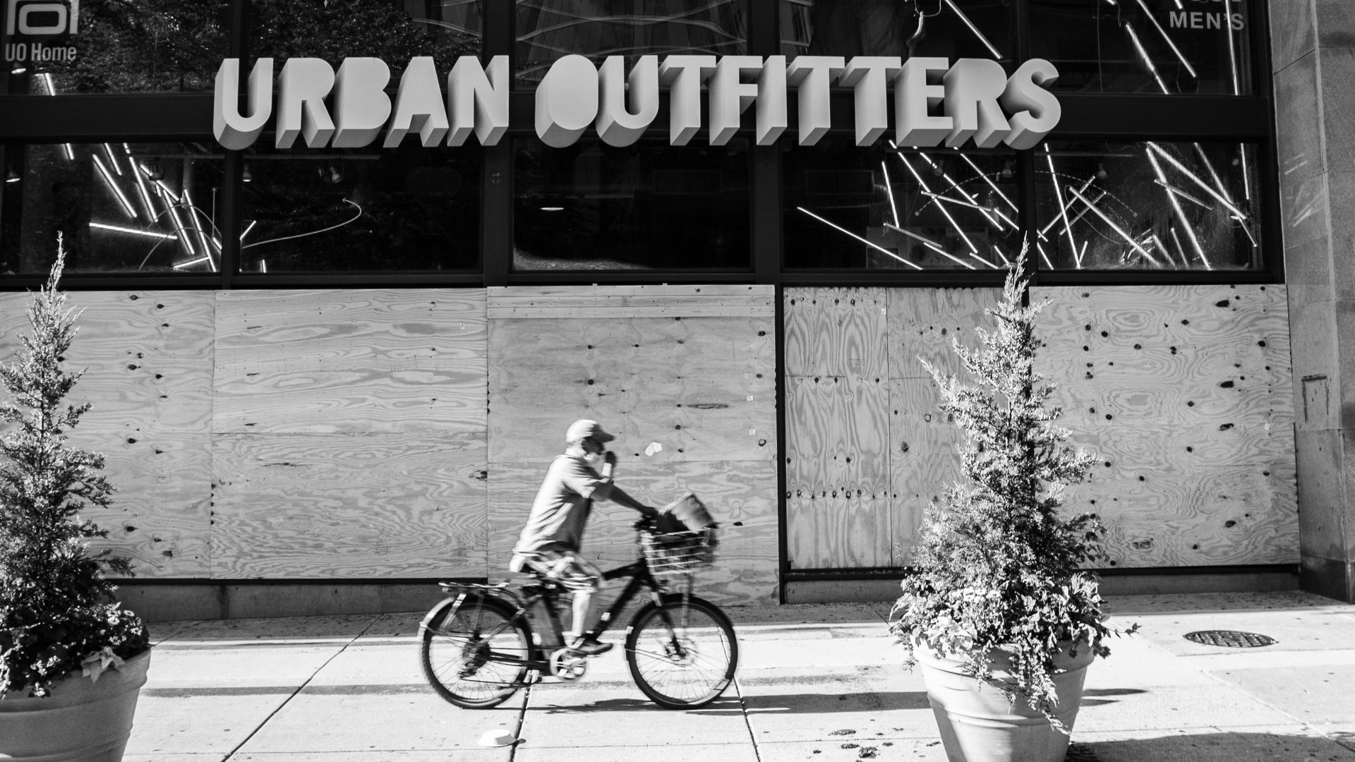 grayscale photo of girl riding bicycle in front of the UNKs coffee shop