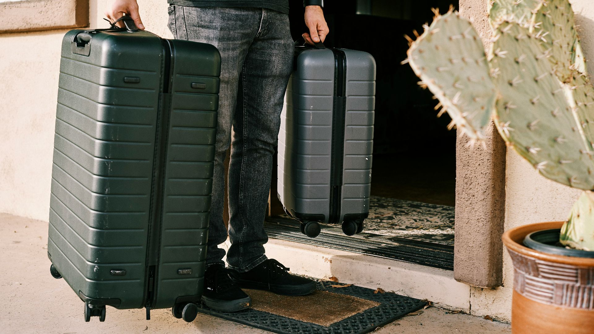 man in black denim jeans and black leather shoes standing beside black luggage bag
