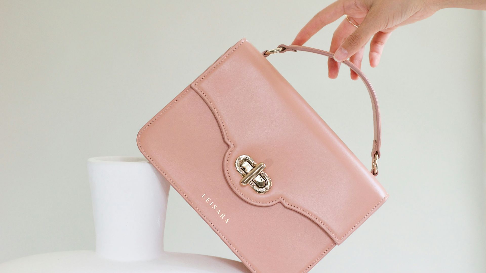 a woman holding a pink purse over a white vase