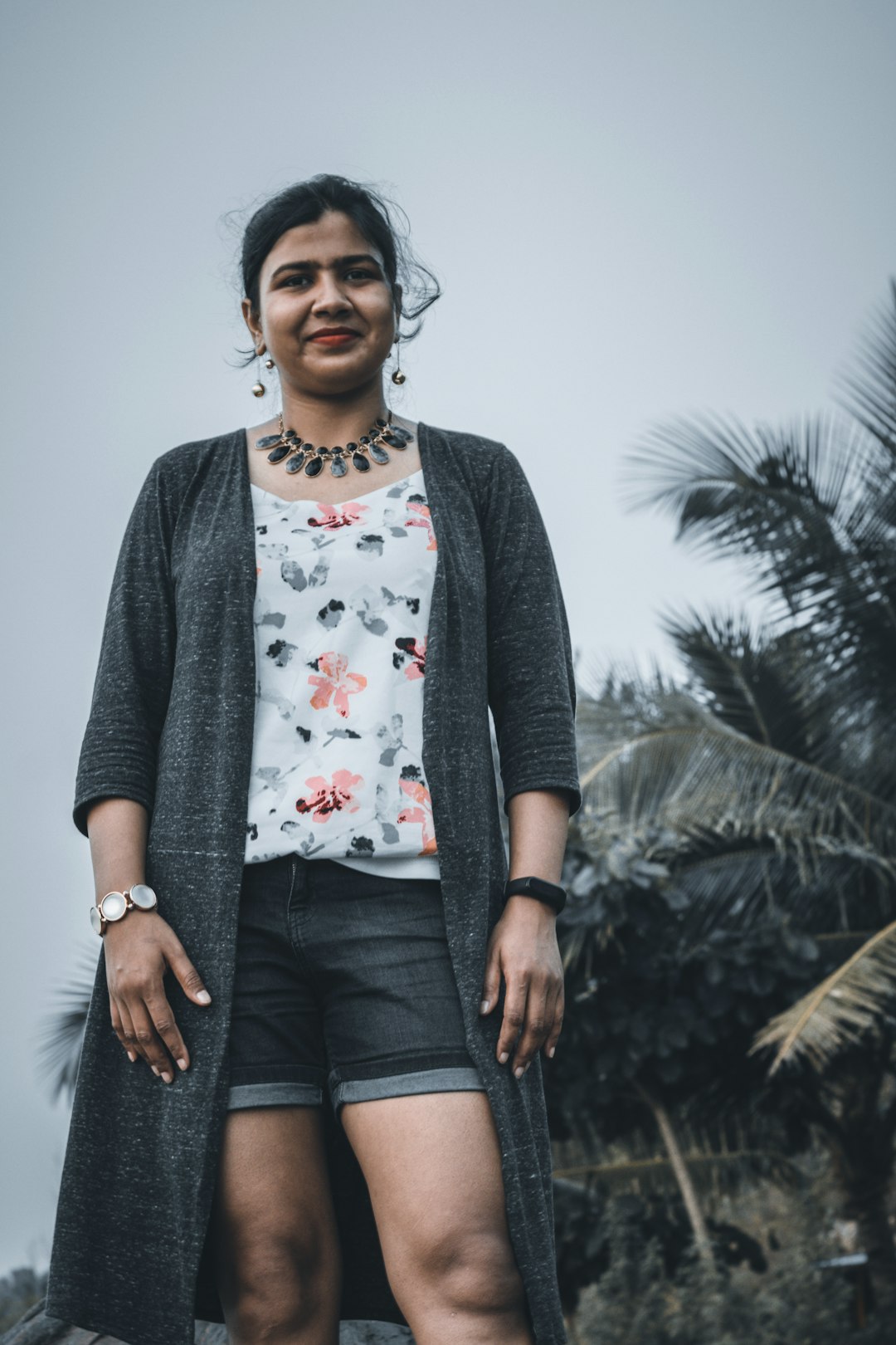 woman in gray cardigan standing near green tree during daytime
