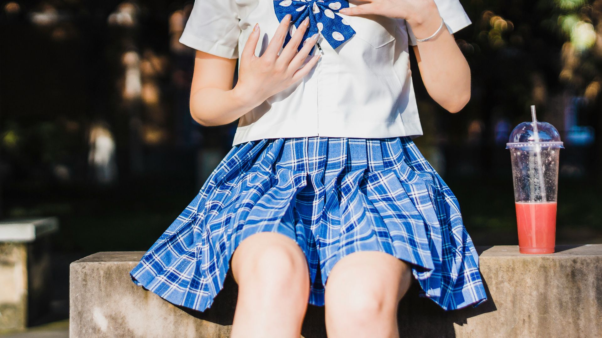 person in white and blue school uniform seating on beach with cup