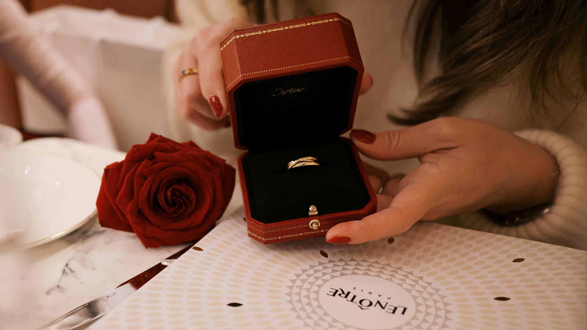 A woman sitting at a table holding a ring box
