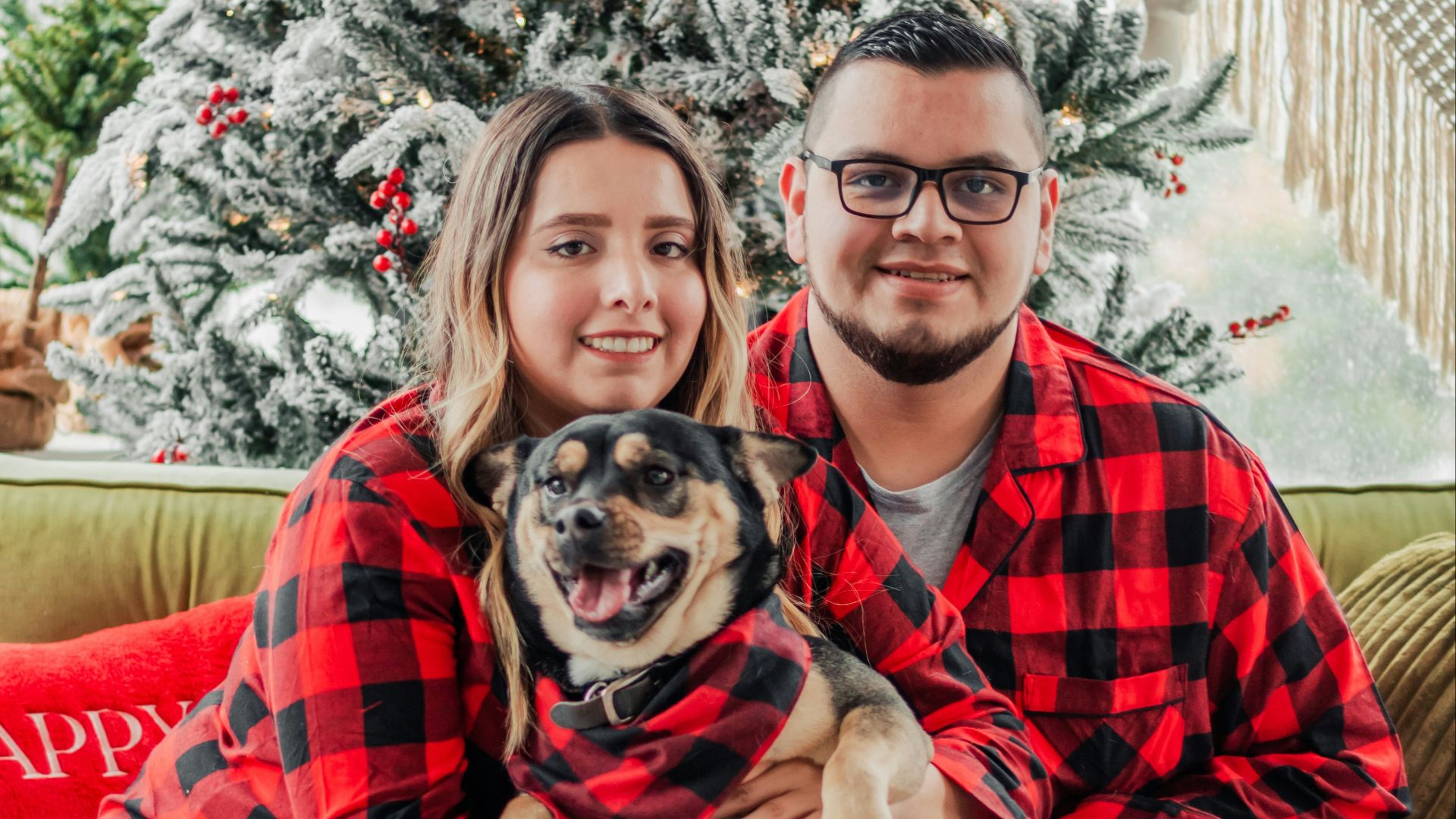 a man and a woman in matching pajamas pose with a dog in front of a