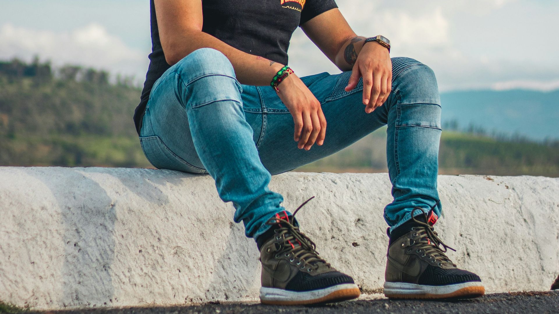 man in black crew neck t-shirt and blue denim jeans sitting on gray concrete wall