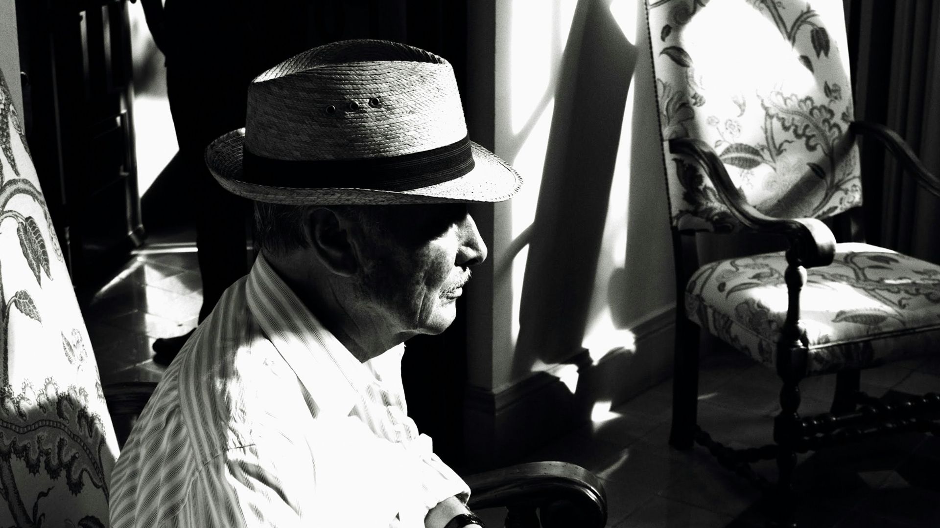 man in white dress shirt and black fedora hat sitting on chair