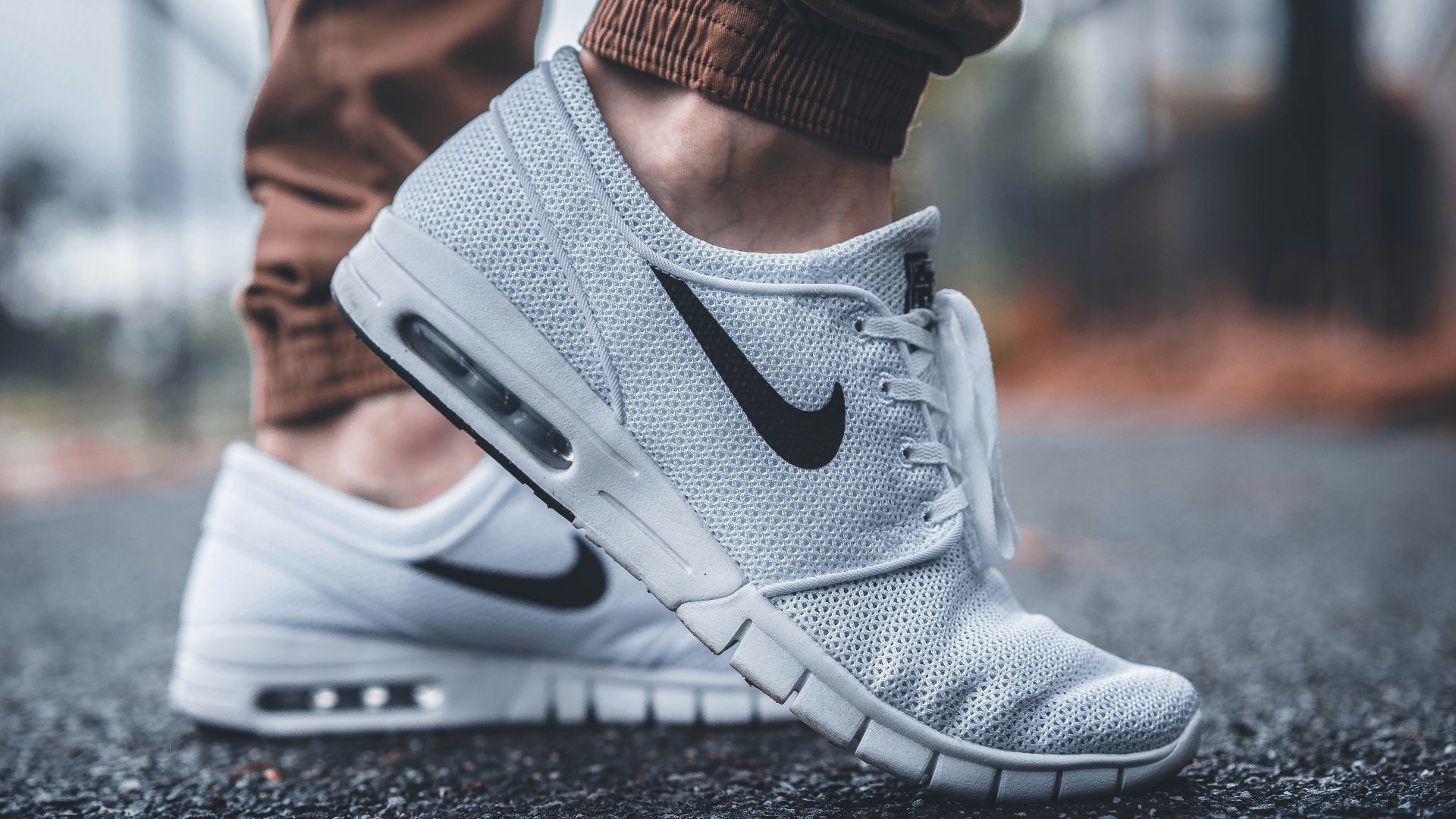 person wearing white Nike running shoes standing on black concrete path