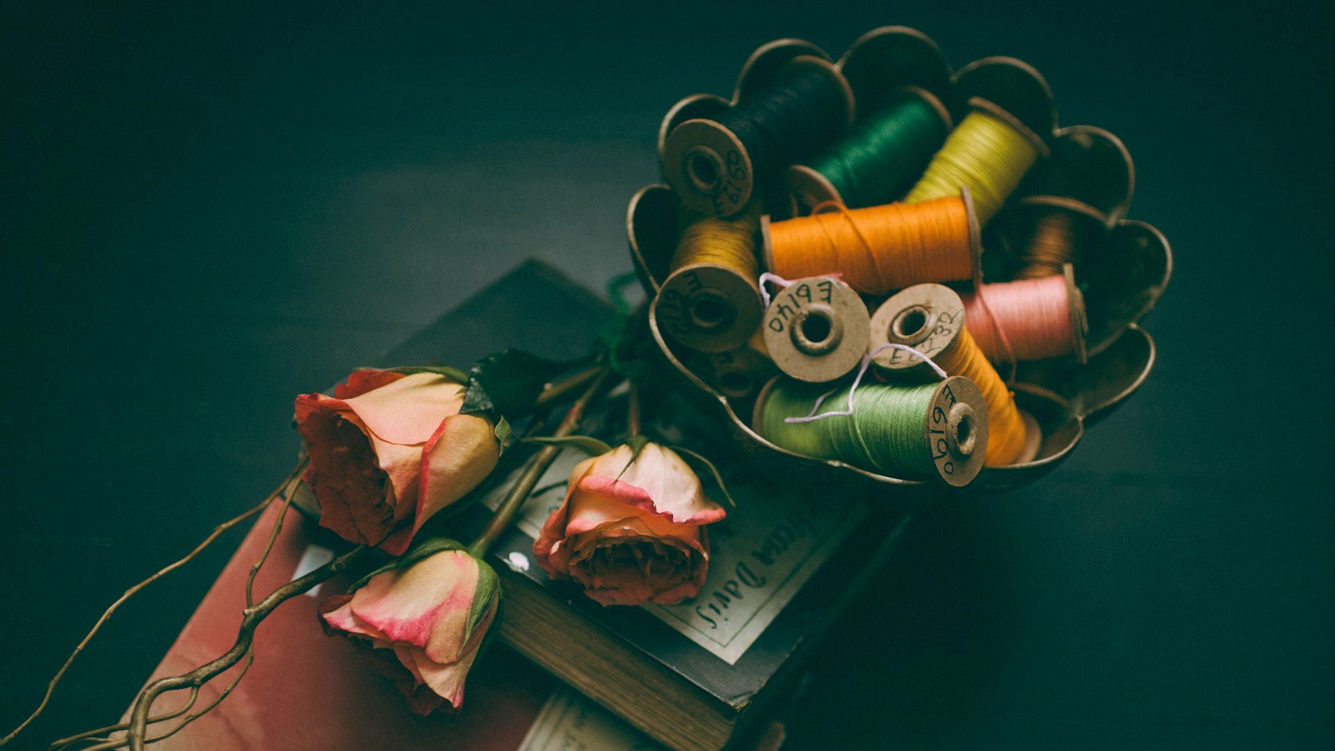 assorted-color thread in bowl beside three roses on two hardbound books