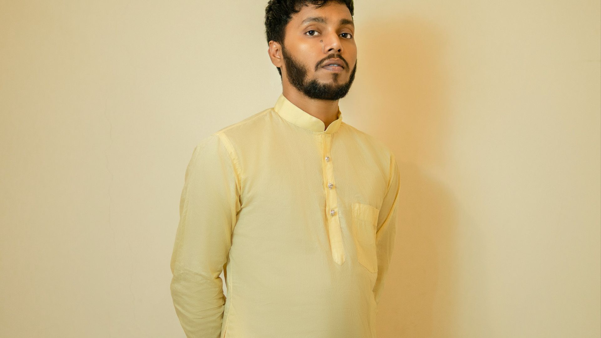 a man standing in front of a wall wearing a yellow shirt