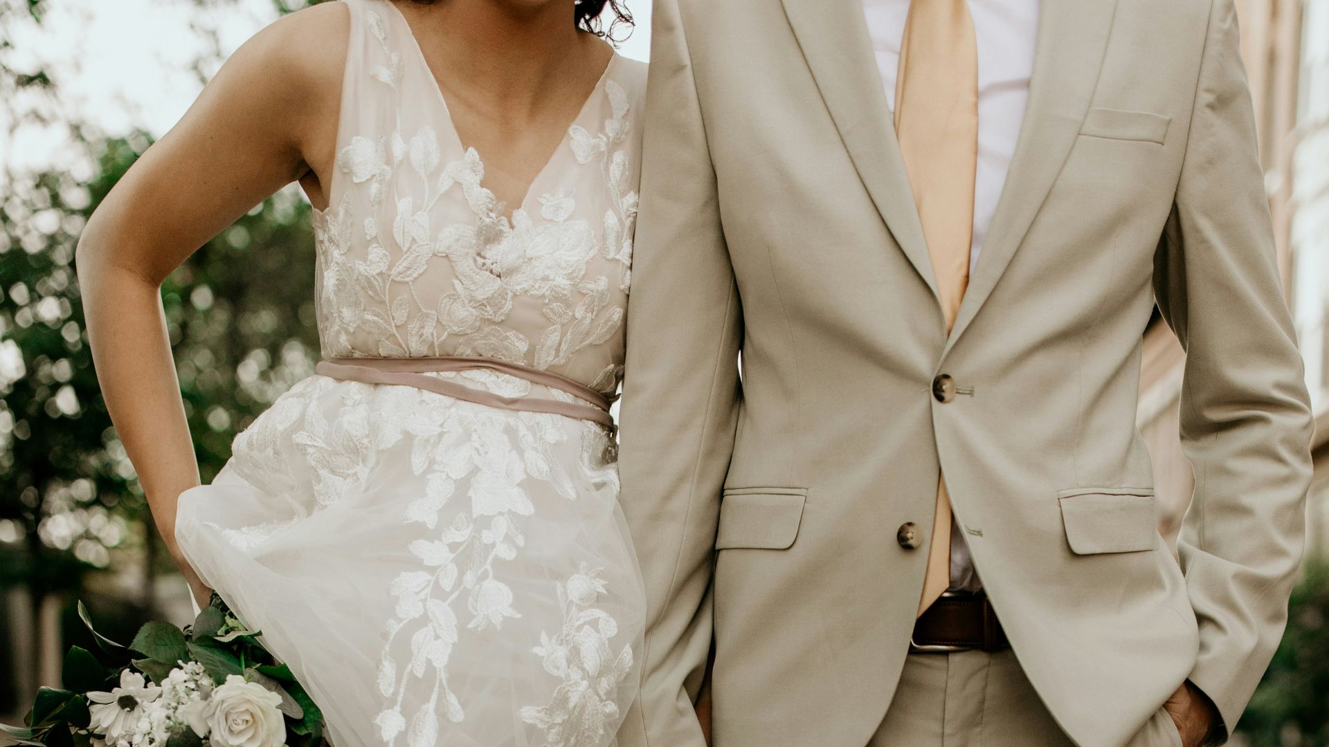 man in gray suit jacket and woman in white wedding dress holding bouquet of white flowers