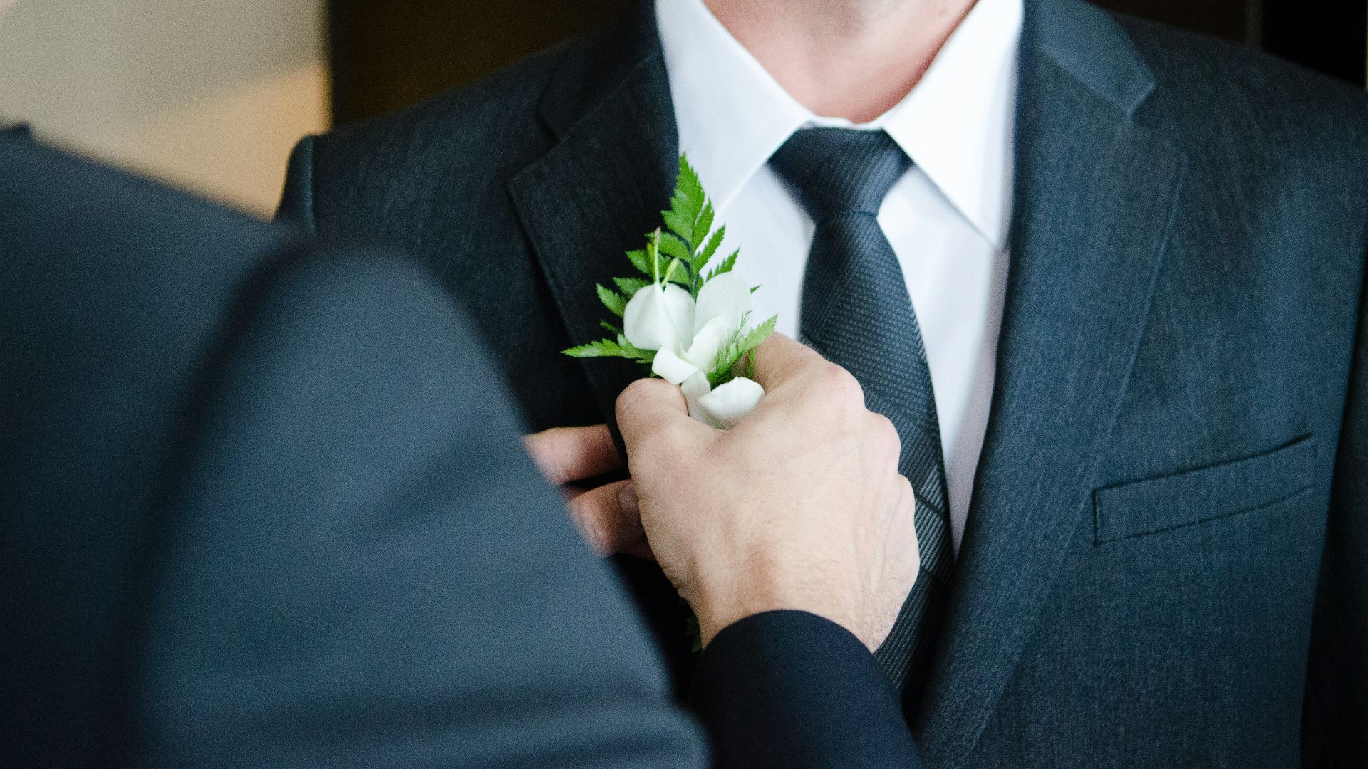 man attaching flower on another man's lapel in a well-lit room