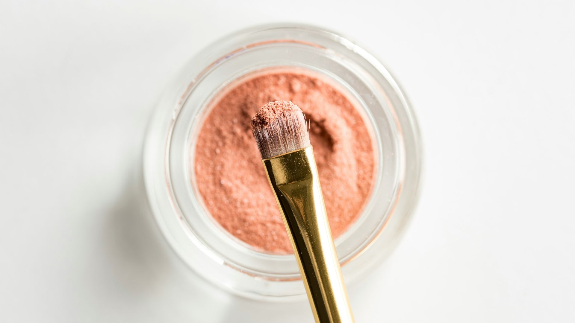 brown makeup brush in front pink powder on glass case