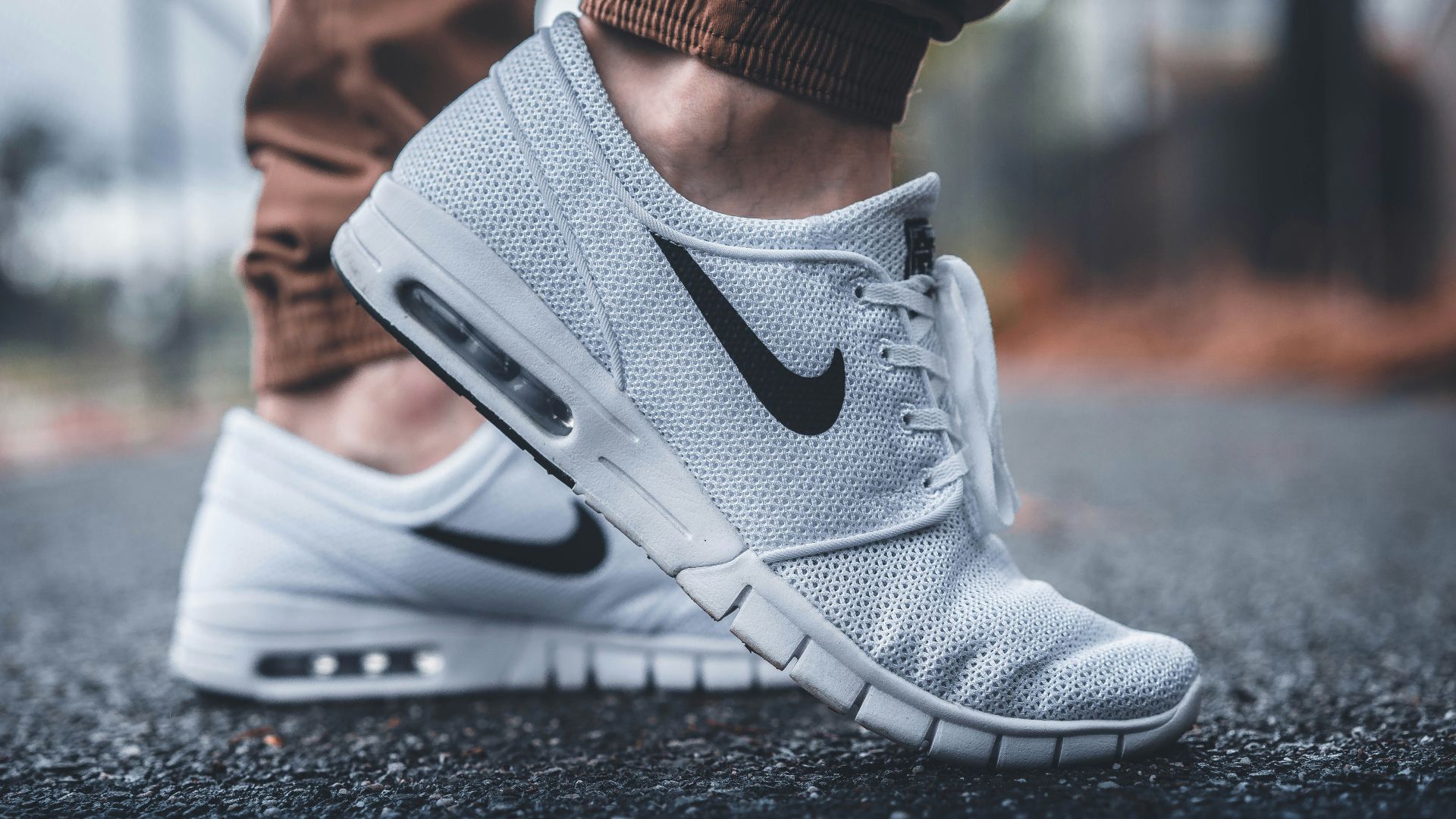 person wearing white Nike running shoes standing on black concrete path