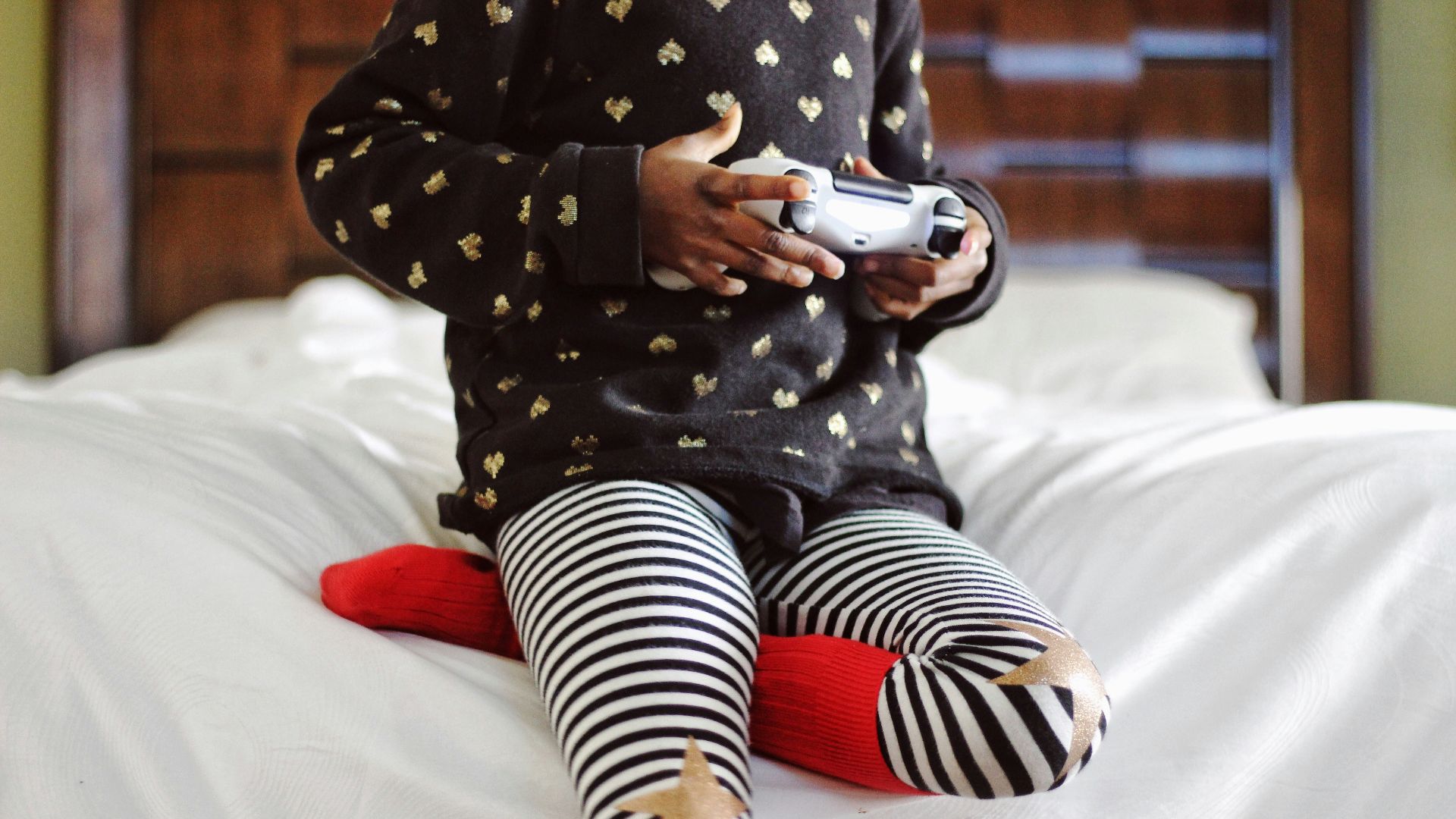 children holding gray game controller sitting on white bed