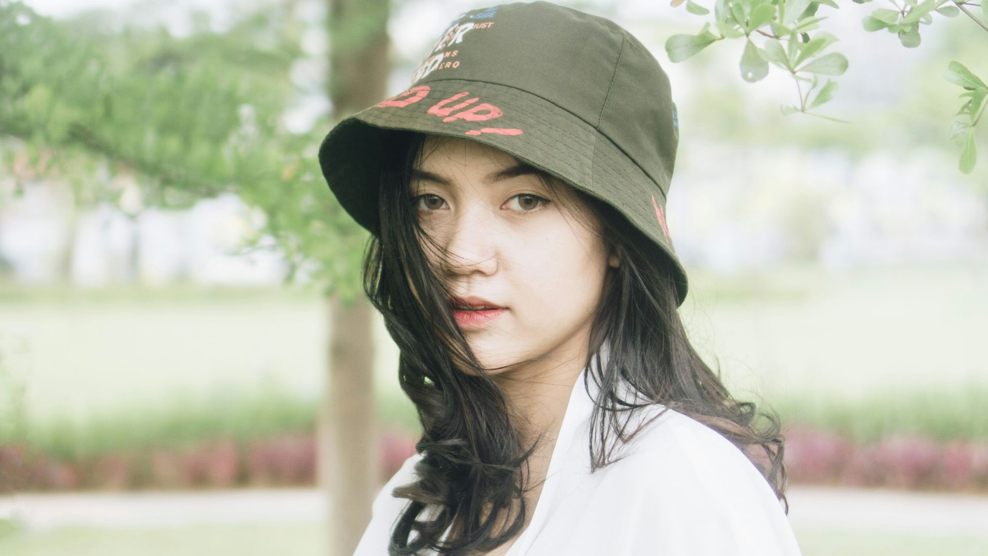a woman wearing a hat standing under a tree