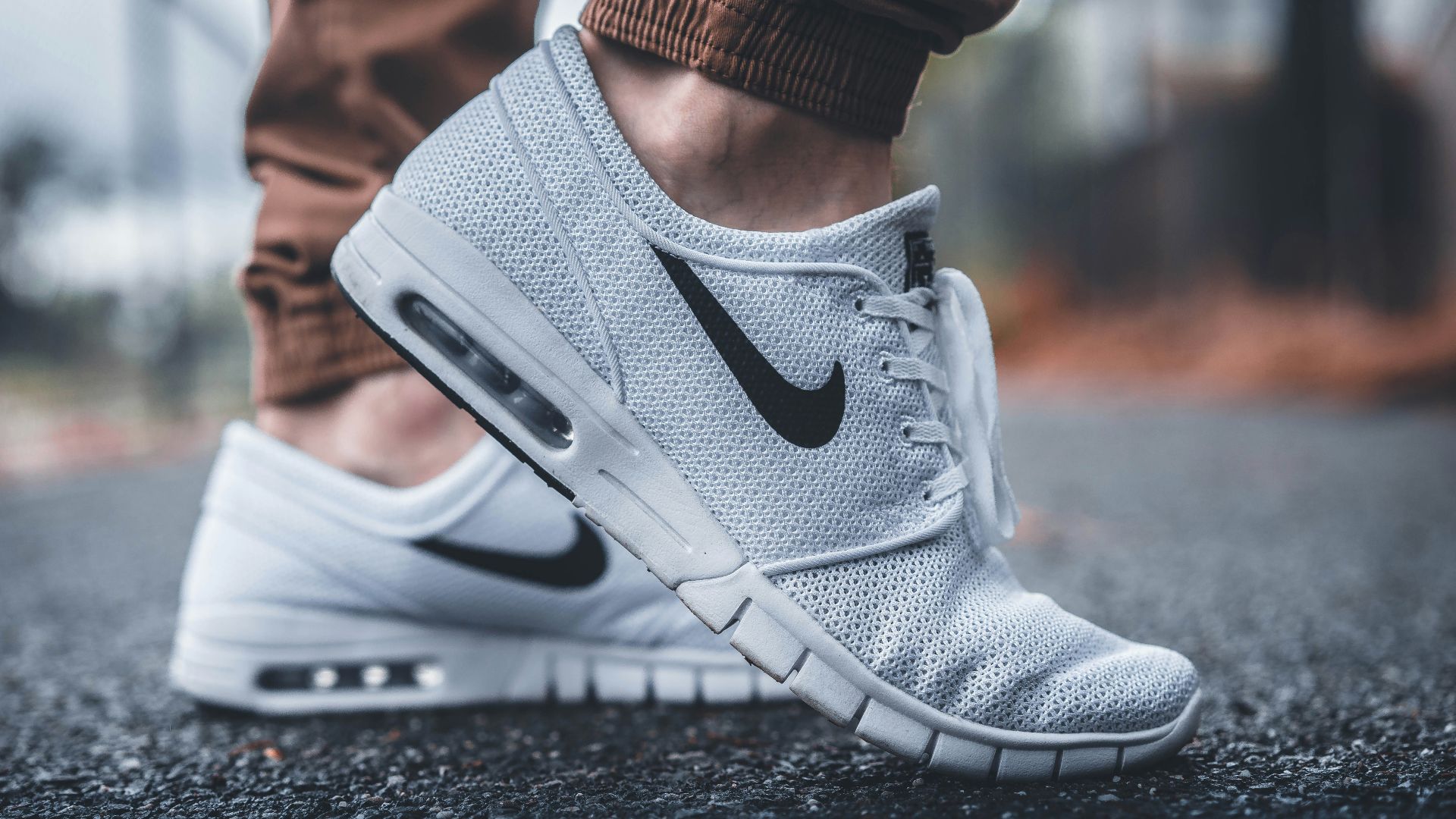 person wearing white Nike running shoes standing on black concrete path