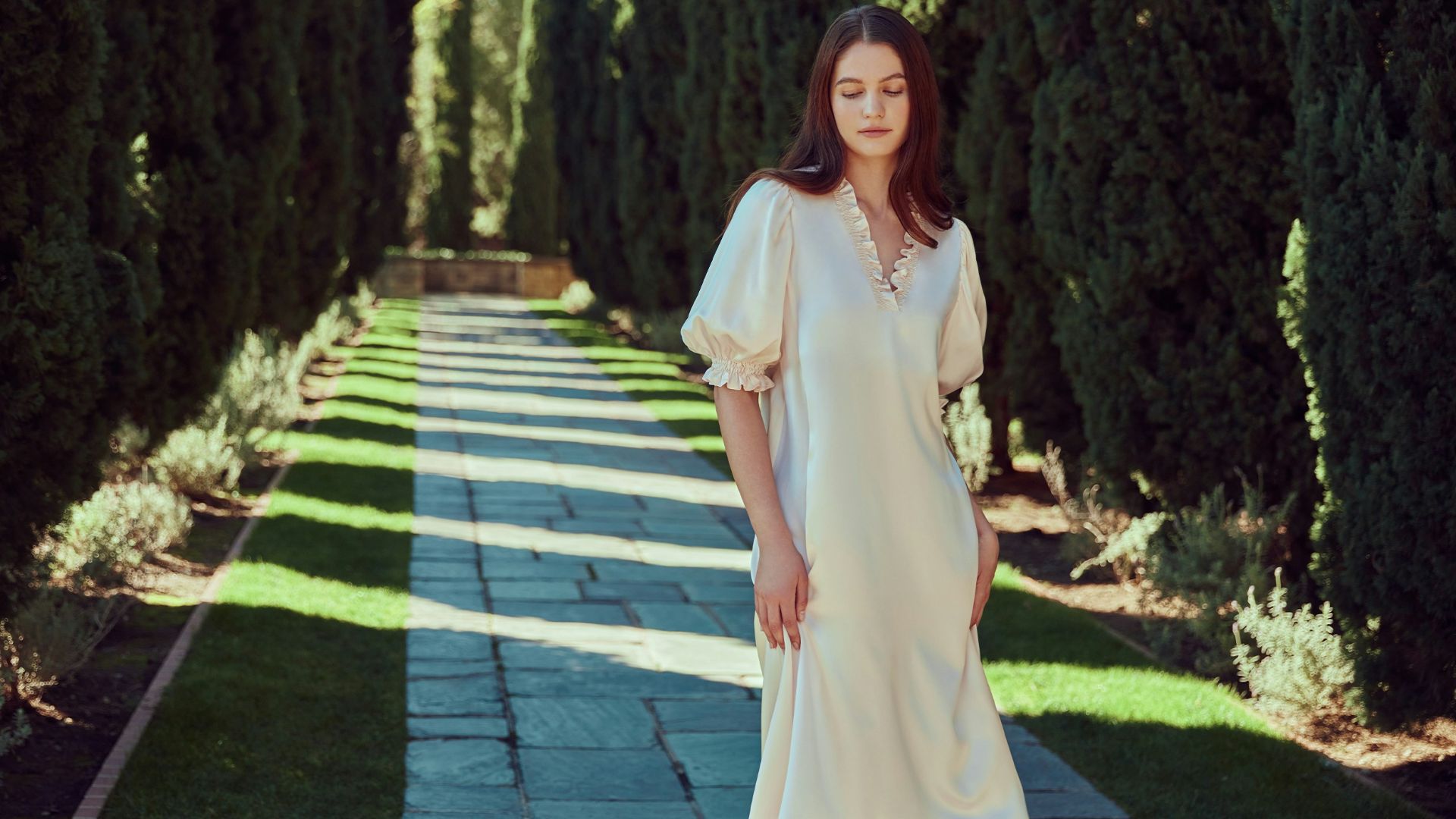 A woman poses in a garden pathway.