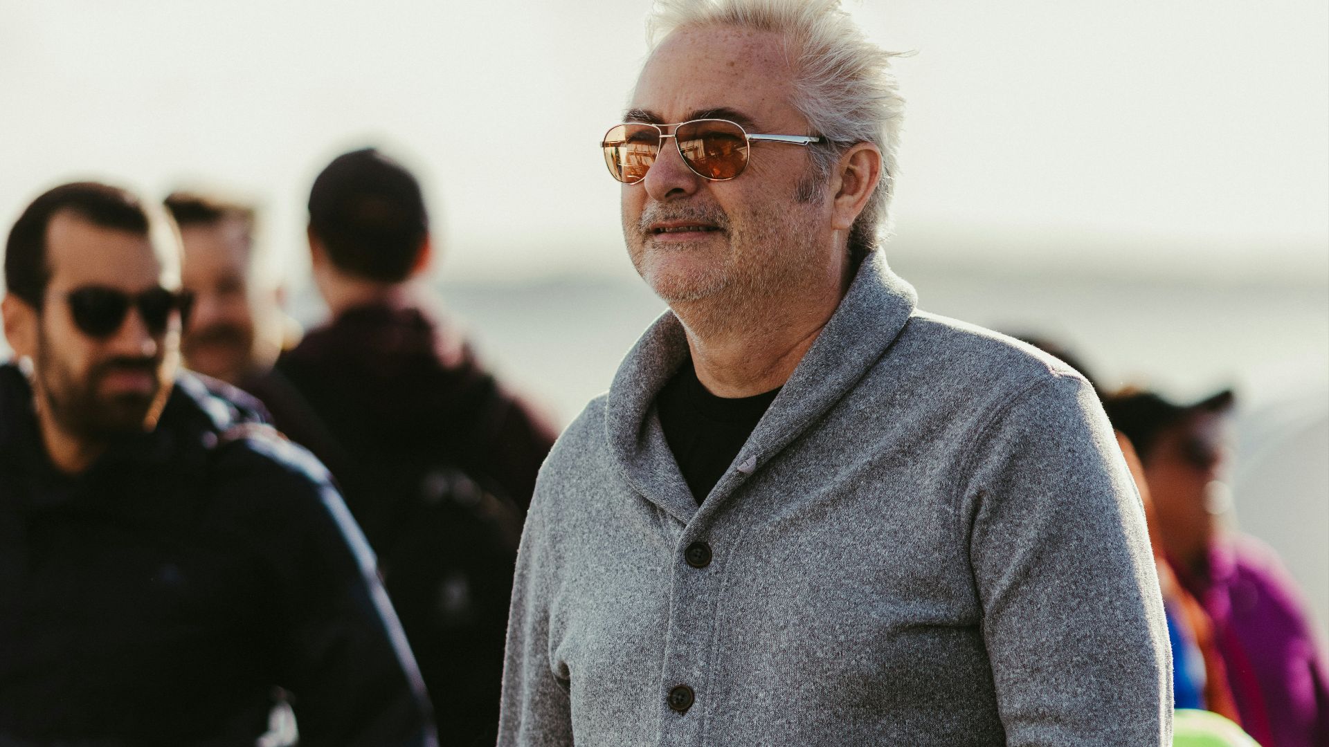 Man with gray cardigan and sunglasses watches event