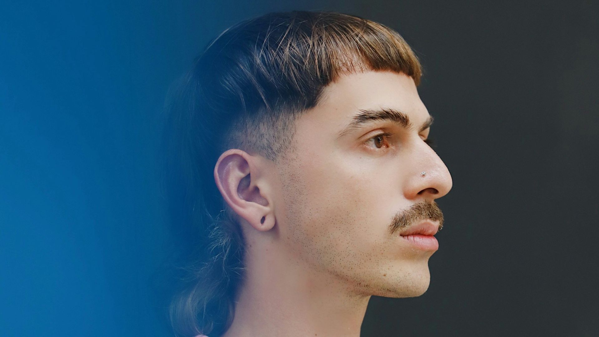 a man with a moustache standing in front of a blue wall