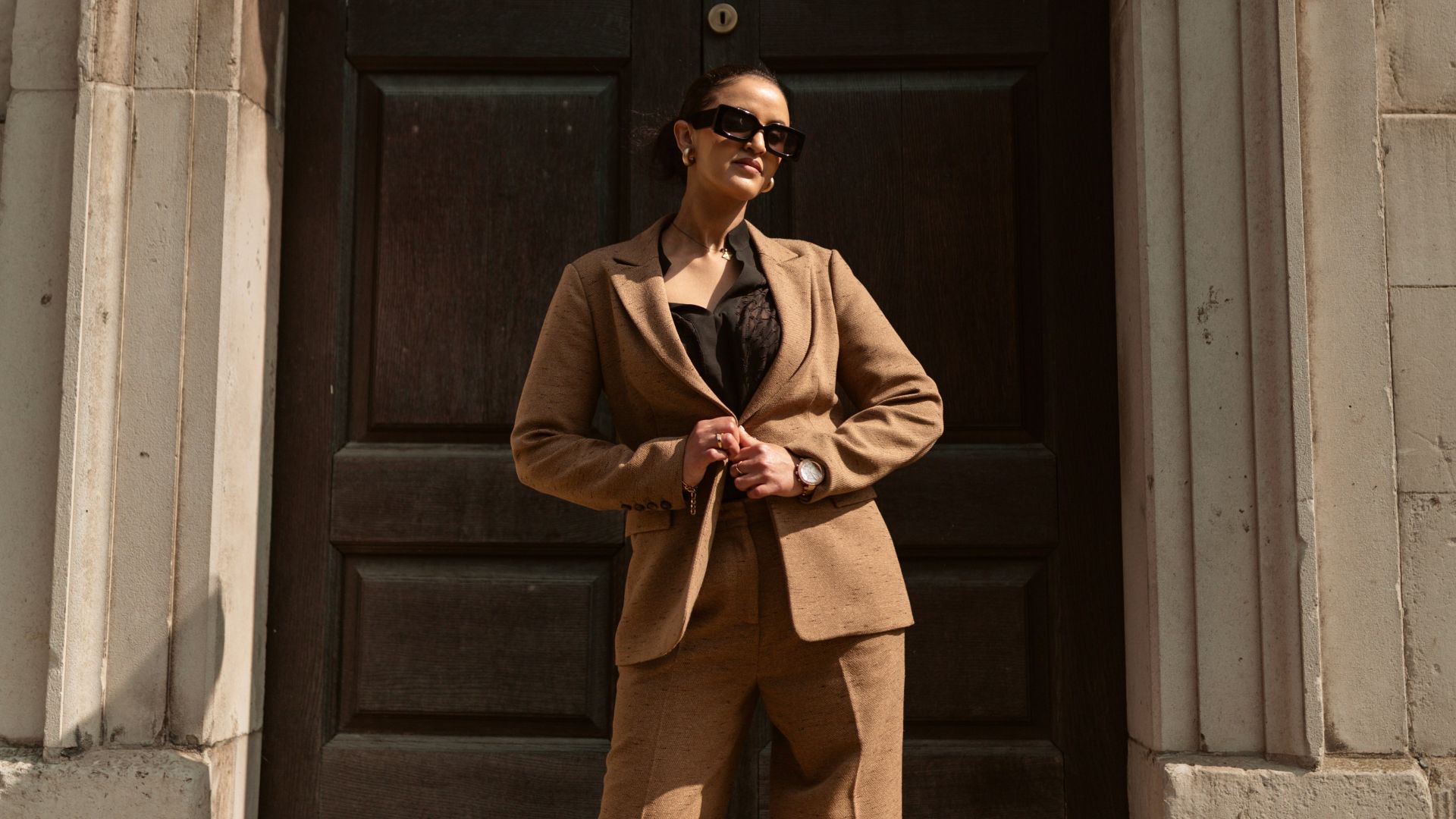 A stylish woman in a brown pantsuit poses.