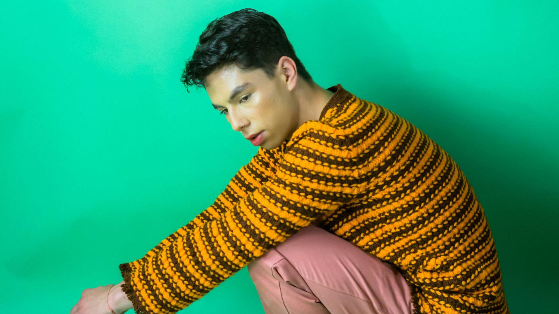 a young man squatting on a stool in front of a green background