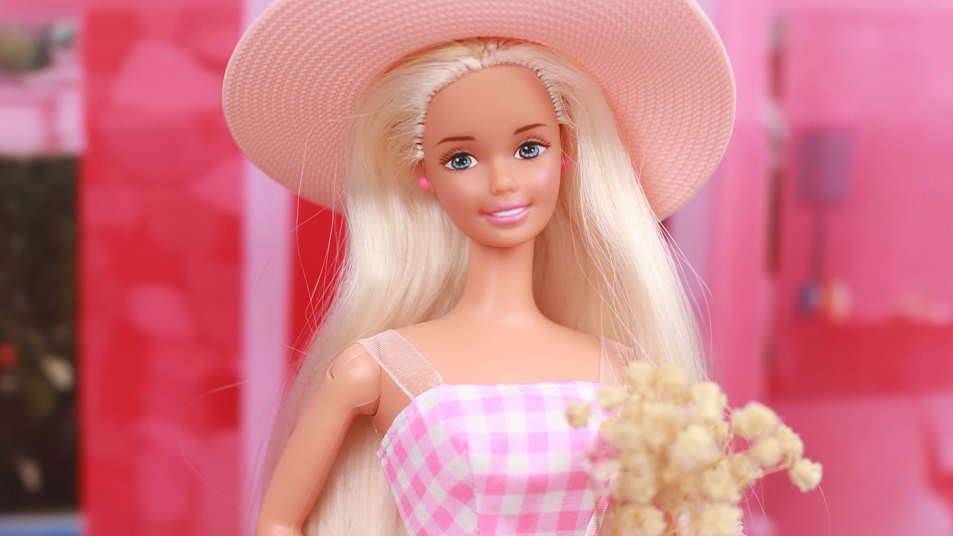 A barbie doll in a pink dress and hat on a pink motorcycle
