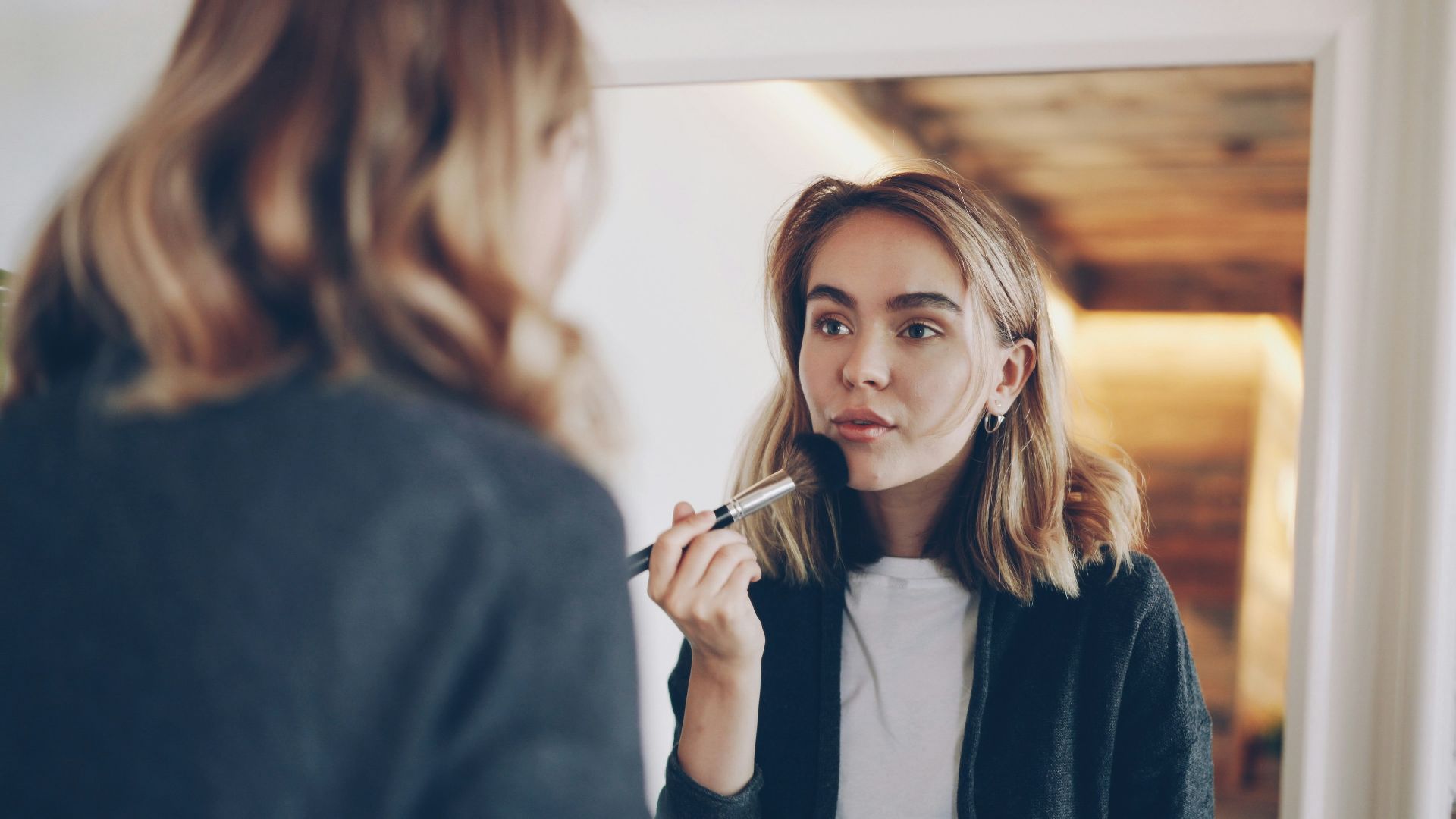 Woman applying makeup in front of a mirror.