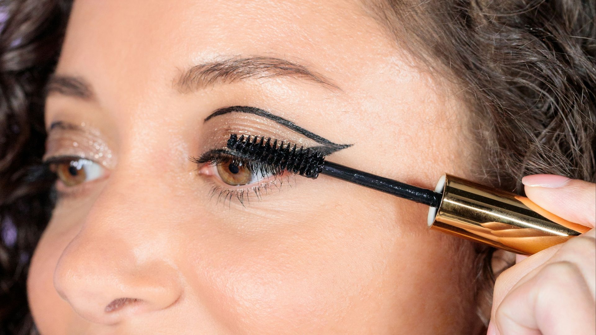 woman with black hair holding brown and black makeup brush