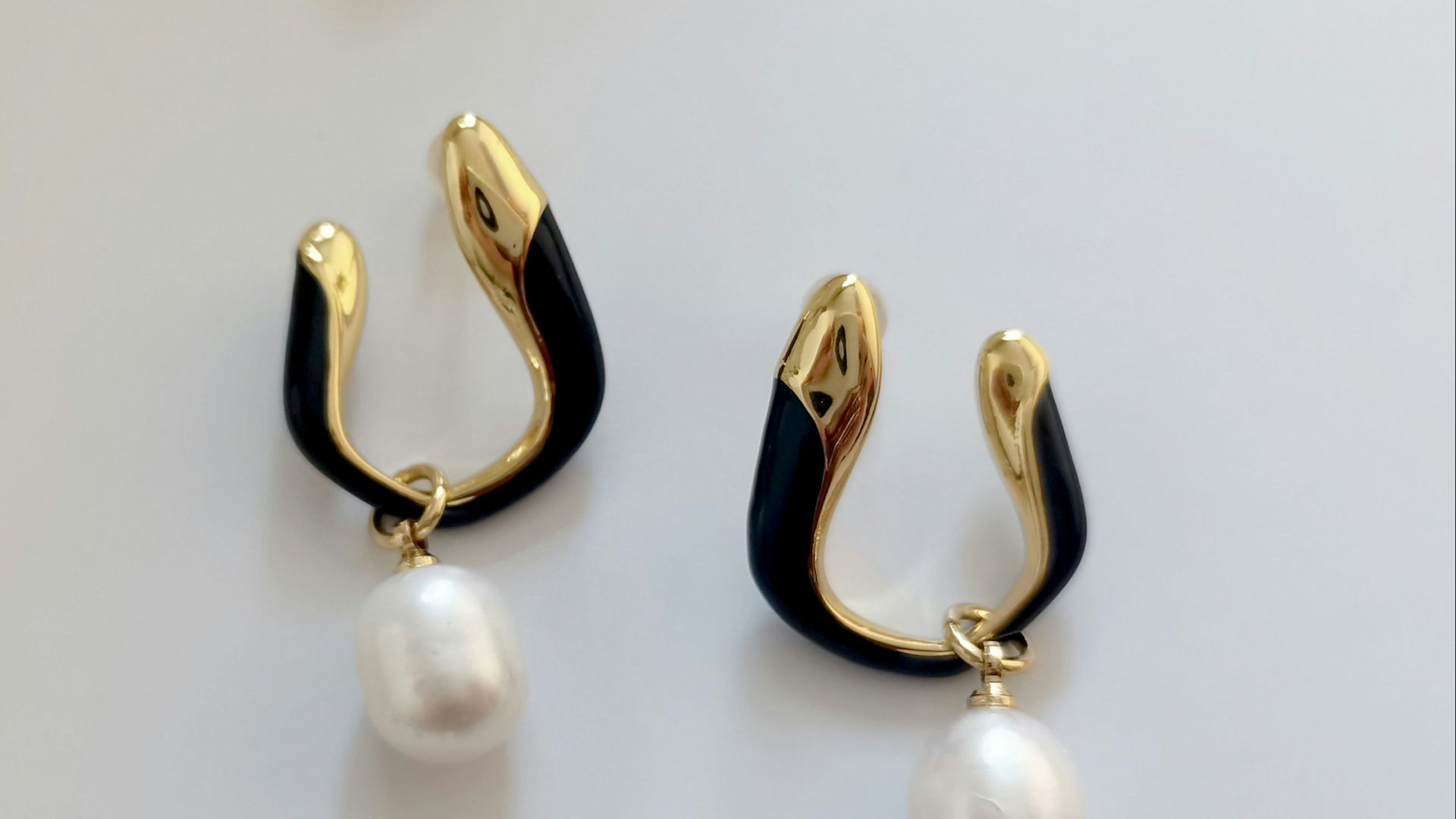 a pair of black and gold earrings with a pearl