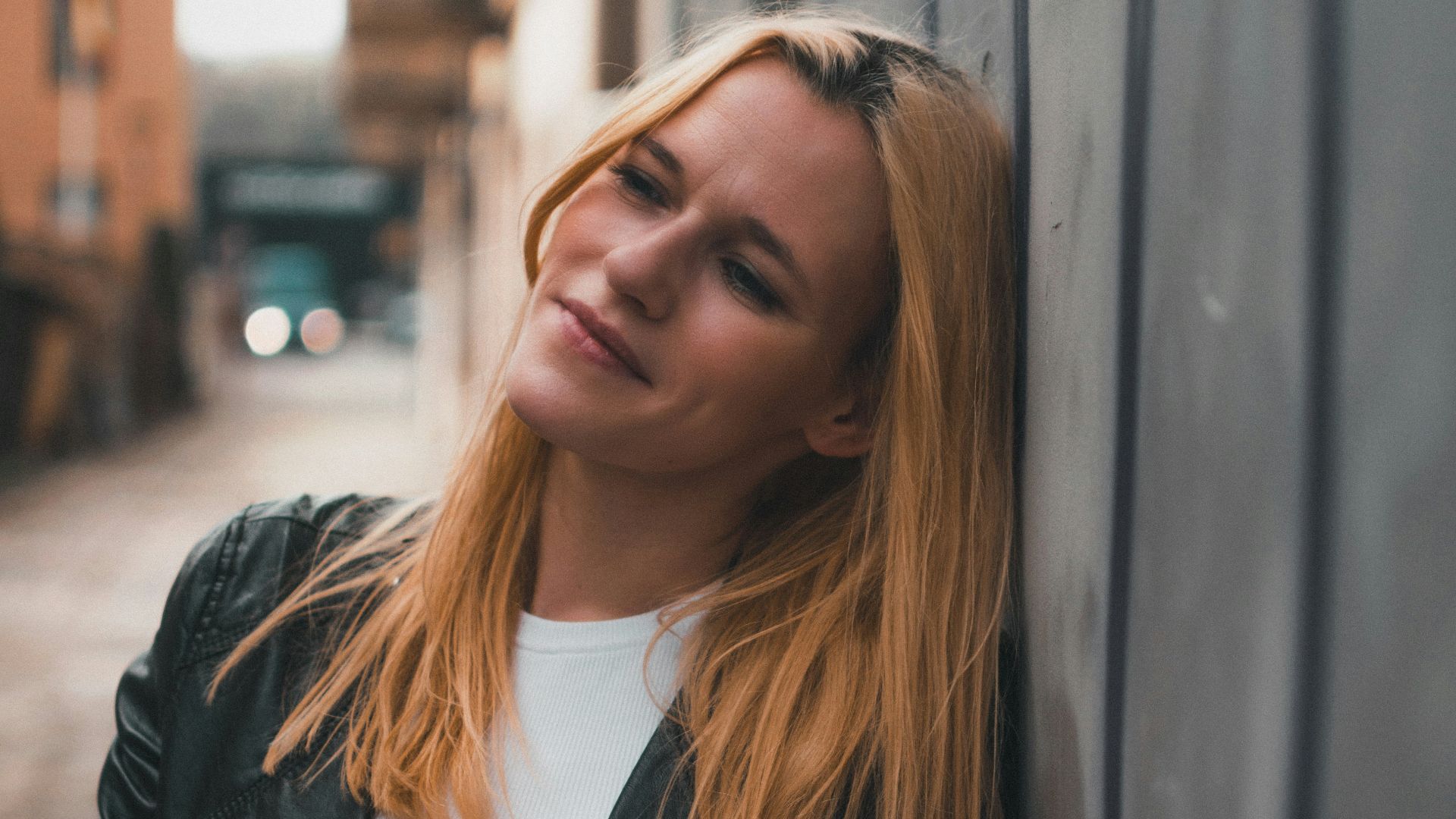 a woman leaning against a wall with her hand on her purse