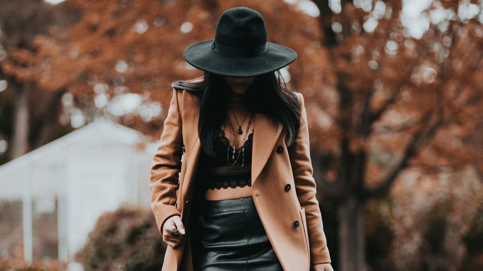 woman in brown coat and black skirt wearing black hat standing on brown grass field during